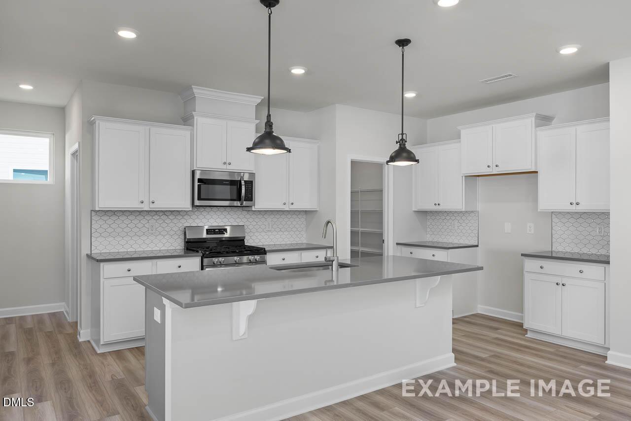 Modern white kitchen with quartz island, stainless appliances, subway tile backsplash in Davidson Homes Adalynn A, Lillington NC