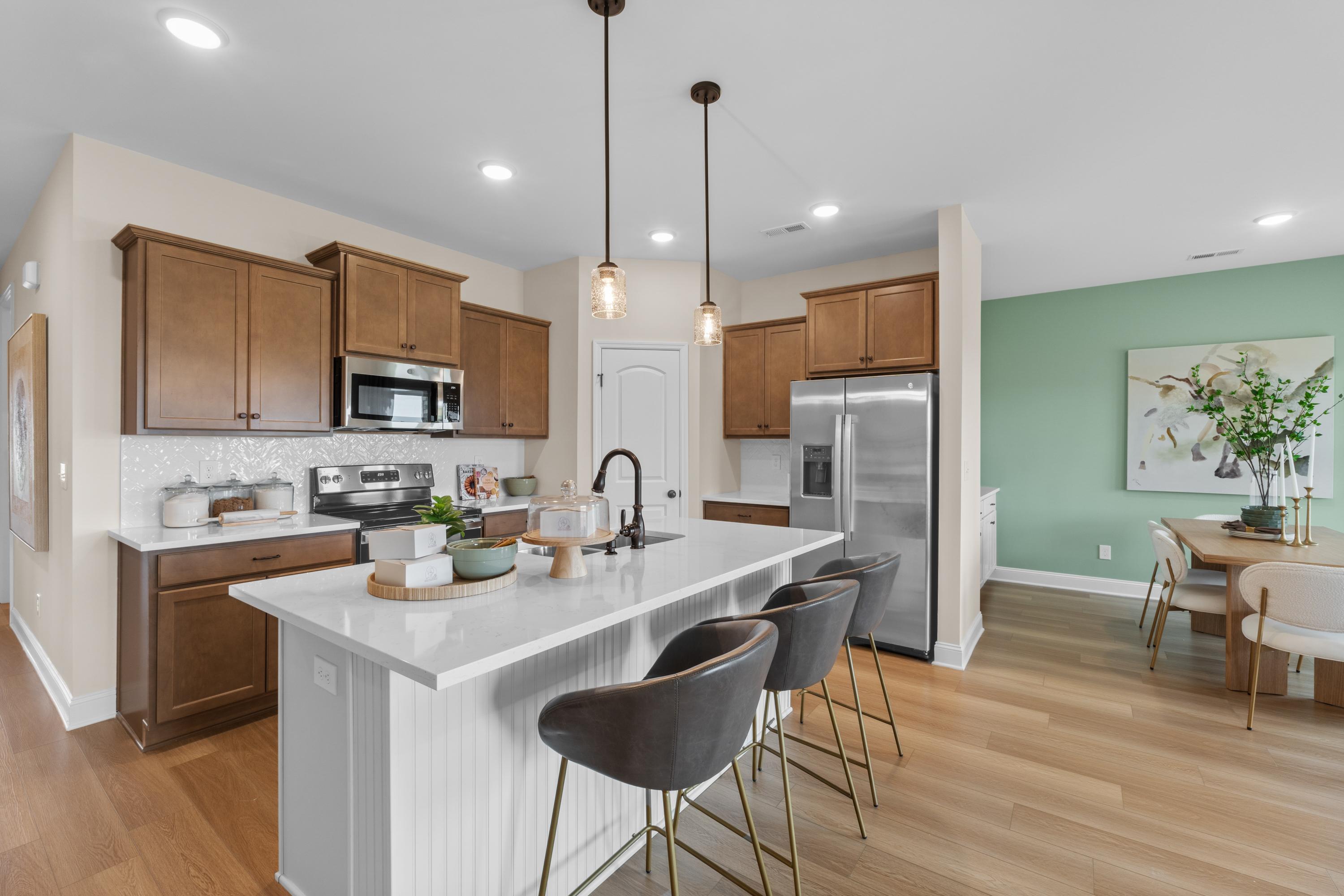 Modern kitchen in The Daphne F showcasing white quartz island, shaker cabinets, stainless appliances, and open dining nook