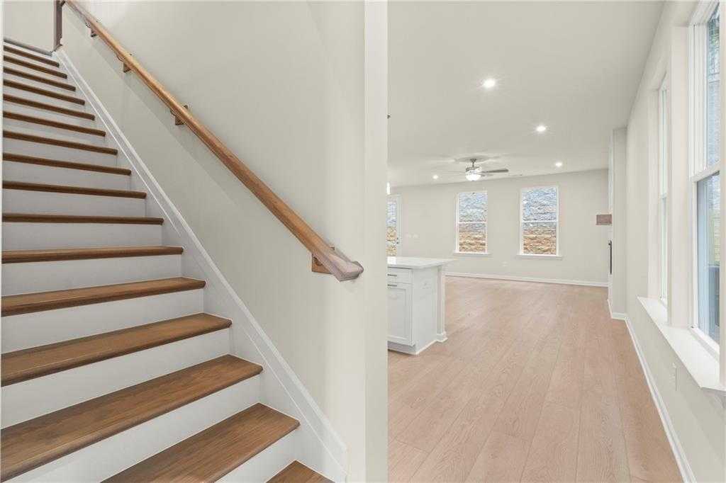 Elegant oak staircase with white railing in bright hallway, open to hardwood floors, large windows, and kitchen island in Davidson Homes Cary A, Kennesaw GA