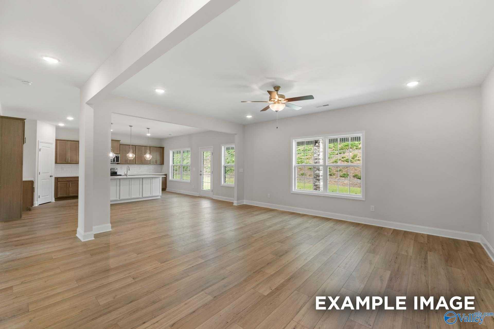 Open-concept living and kitchen area with hardwood floors, white cabinets, island, large windows, and ceiling fan in Davidson Homes The Madison A, Meridianville, Alabama