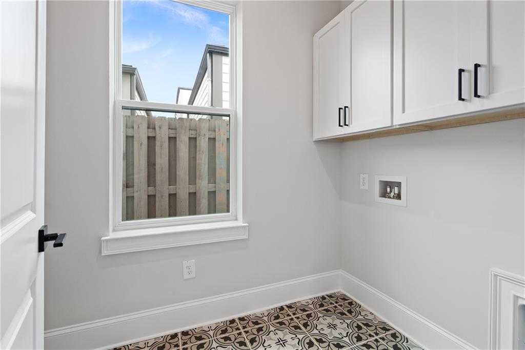 Bright laundry room with white cabinets, patterned tile floor, utility sink, and window to fenced backyard in Davidson Homes The Seaside B, Woodstock, GA