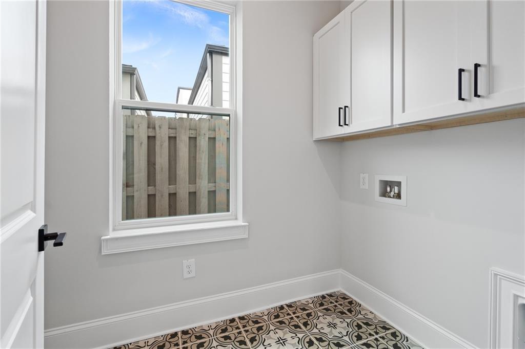 Bright laundry room with white cabinets, patterned tile floor, utility sink, and window to fenced backyard in Davidson Homes The Seaside B, Woodstock, GA