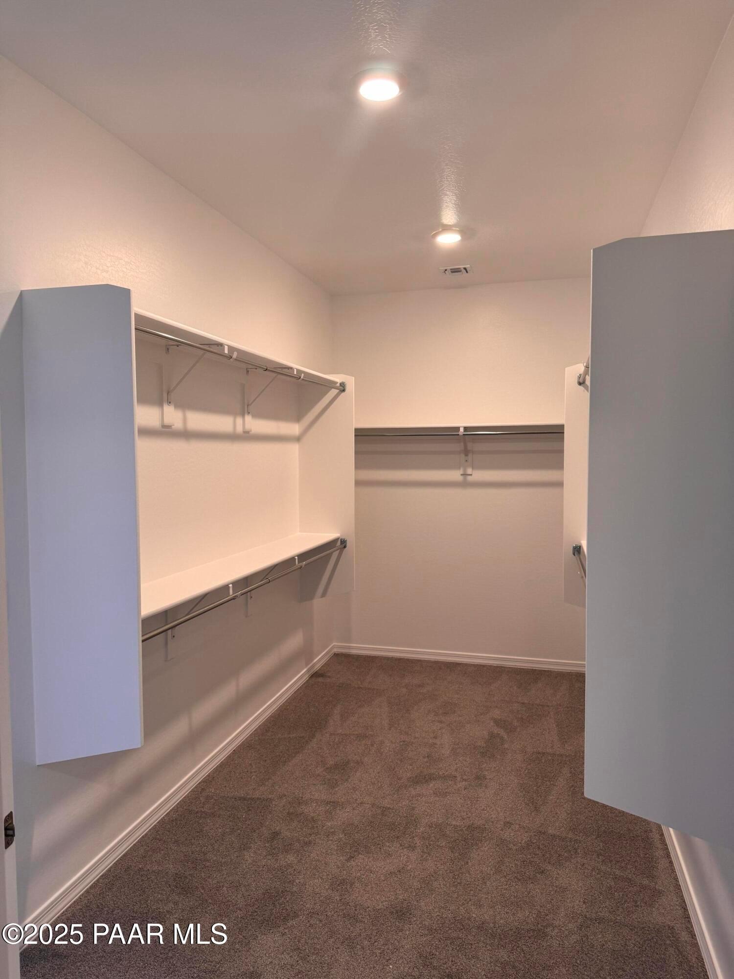 Spacious walk-in closet with white walls, built-in shelves, and hanging rods on carpeted floor in Davidson Homes Sunrise II A, Prescott AZ