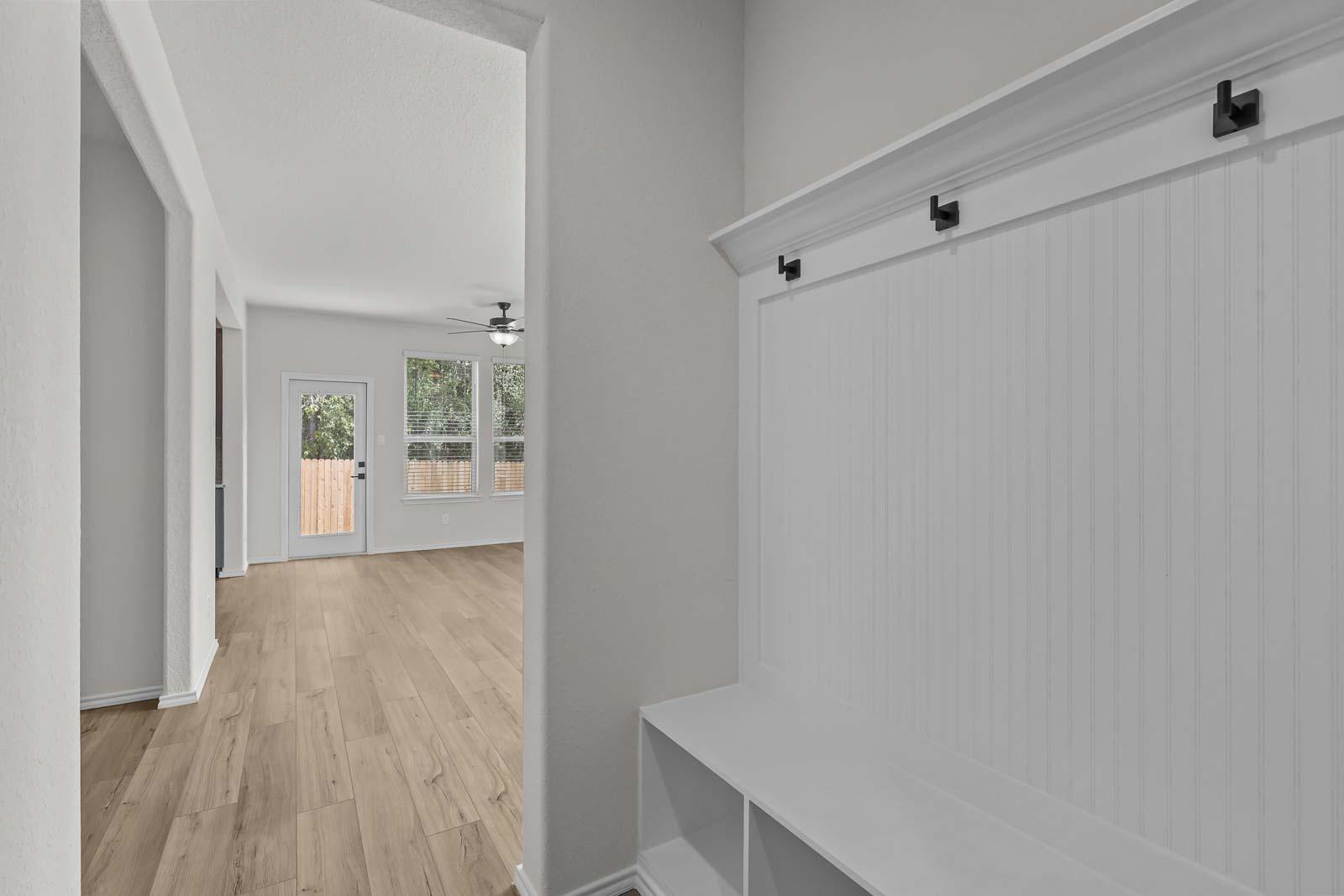 Mudroom drop zone in The Florence B featuring white beadboard wall paneling and built-in storage bench with hooks.