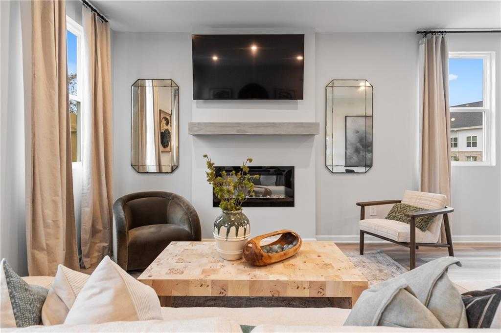 Cozy living room with gas fireplace, mounted TV, decorative mirrors, plush armchairs, and wooden coffee table in Davidson Homes Wilmington B, Emerson, GA
