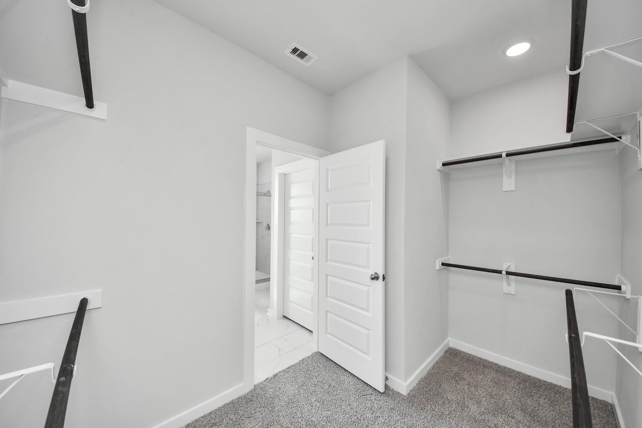 Walk-in closet with shelving and carpeted floors in The Riviera A floor plan at Emberly in Beasley, Texas.