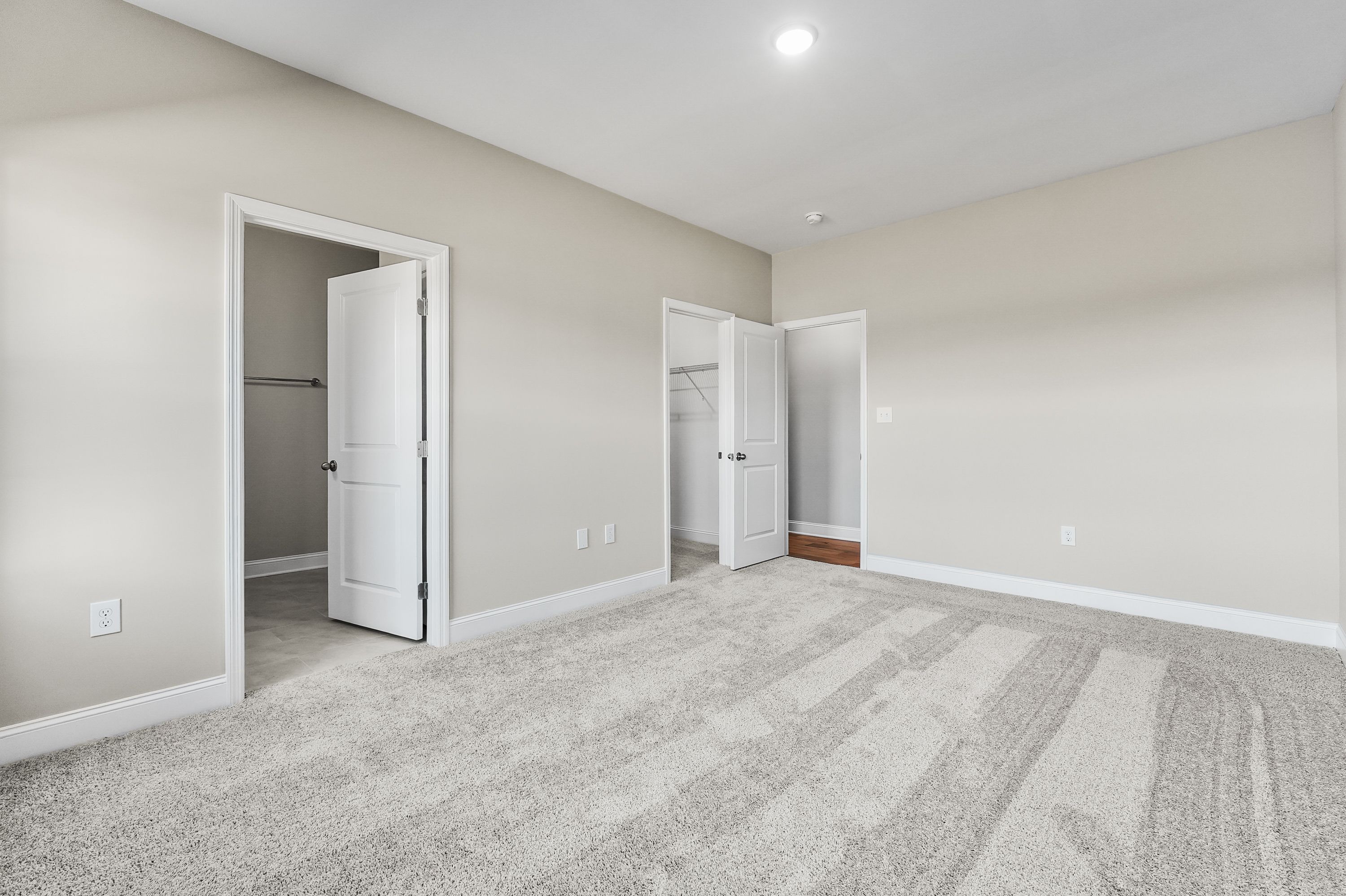 Spacious master bedroom in The Valencia with open walk-in closet door, en-suite access, beige walls, and plush gray carpet