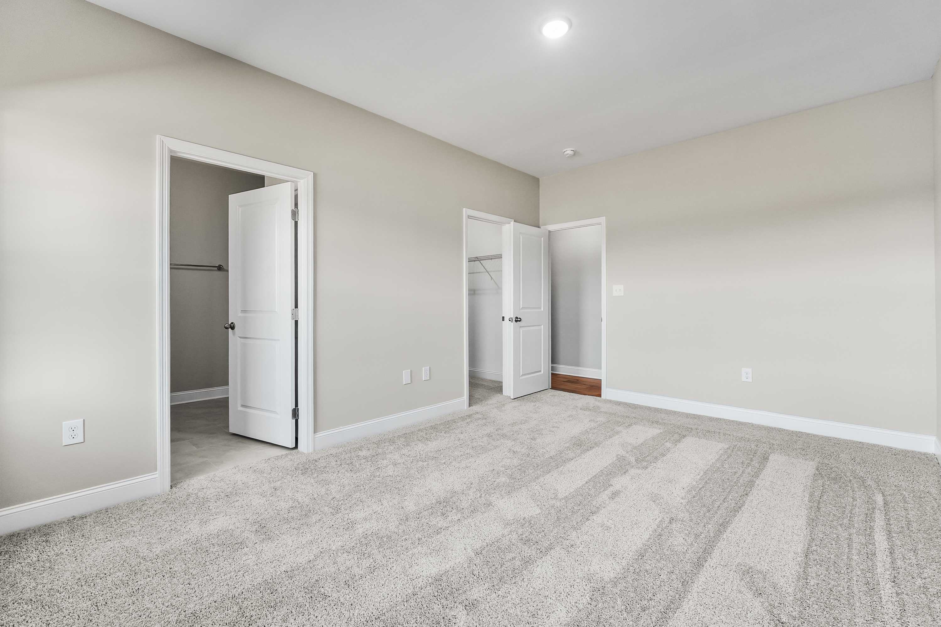 Spacious master bedroom in The Valencia with open walk-in closet door, en-suite access, beige walls, and plush gray carpet