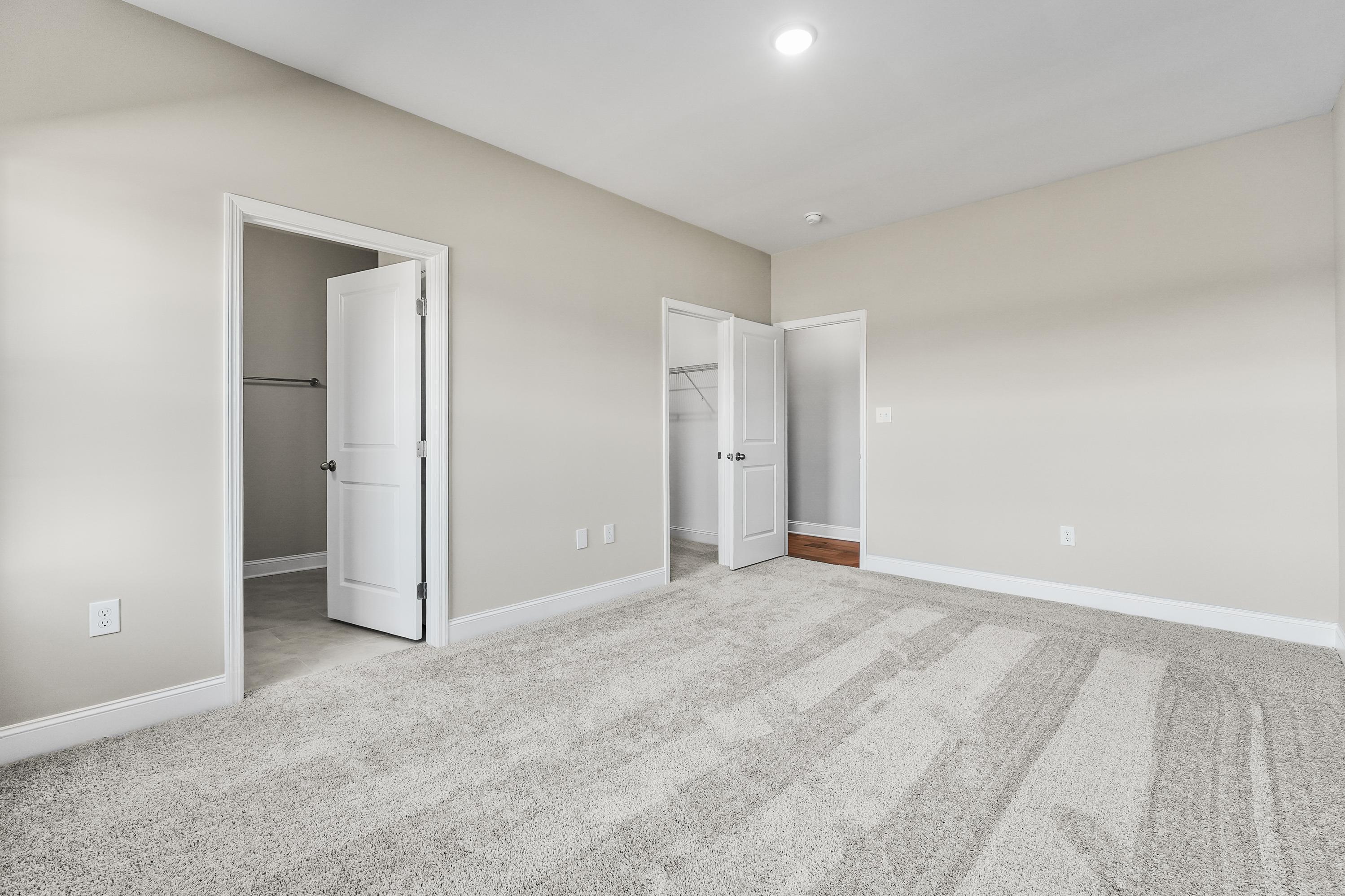 Spacious master bedroom in The Valencia with open walk-in closet door, en-suite access, beige walls, and plush gray carpet