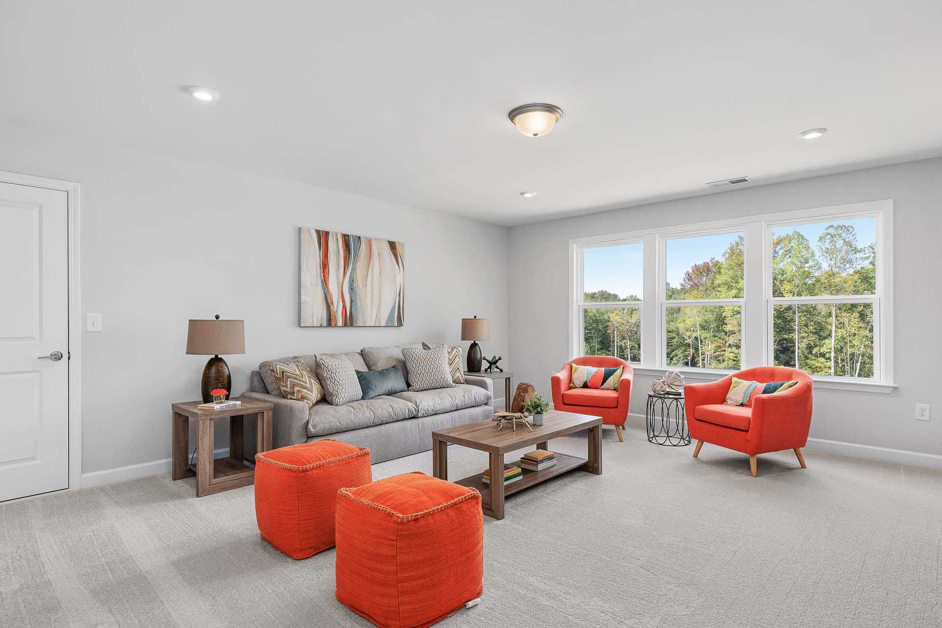Cozy living room in Glenmere by Davidson Homes, Knightdale NC, featuring gray sofa, orange accent chairs, wooden coffee table, and large windows