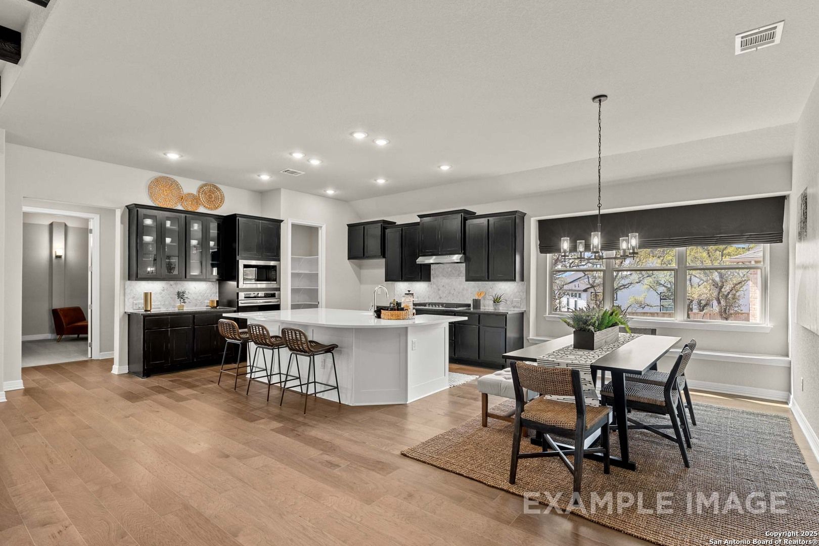 Modern open-concept kitchen with black cabinets, white island, stainless appliances, and dining area in Davidson Homes Summerlin B, Castroville, Texas
