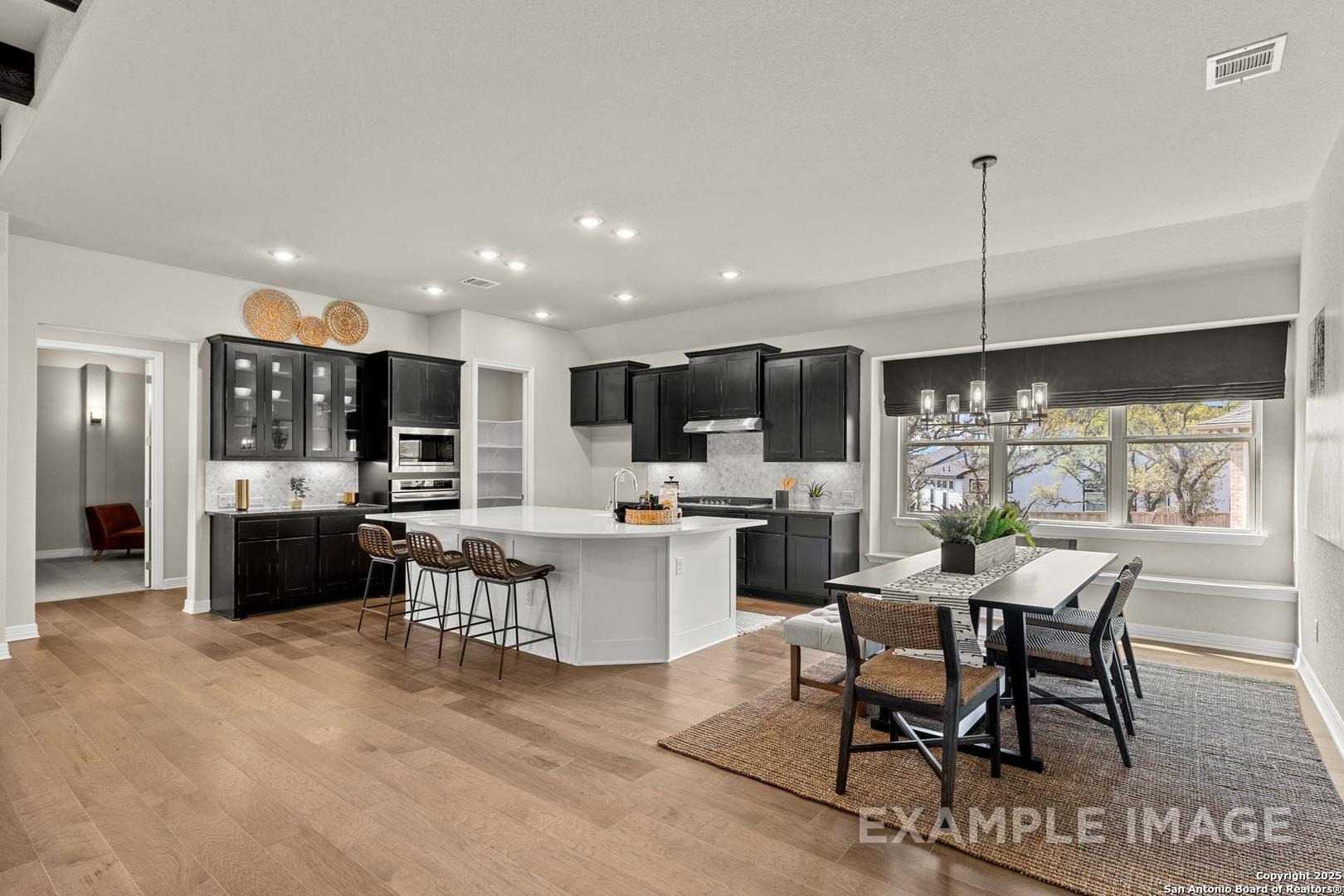 Modern open-concept kitchen with black cabinets, white island, stainless appliances, and dining area in Davidson Homes Summerlin B, Castroville, Texas