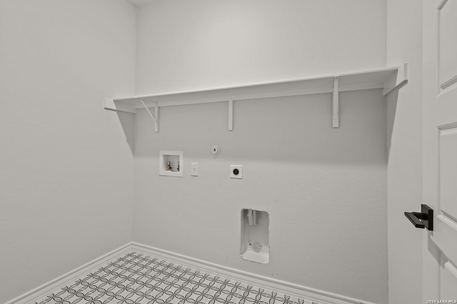 Laundry room with white shelving, patterned tile floor, and washer hookups in Davidson Homes The Oxford F, Castroville, TX