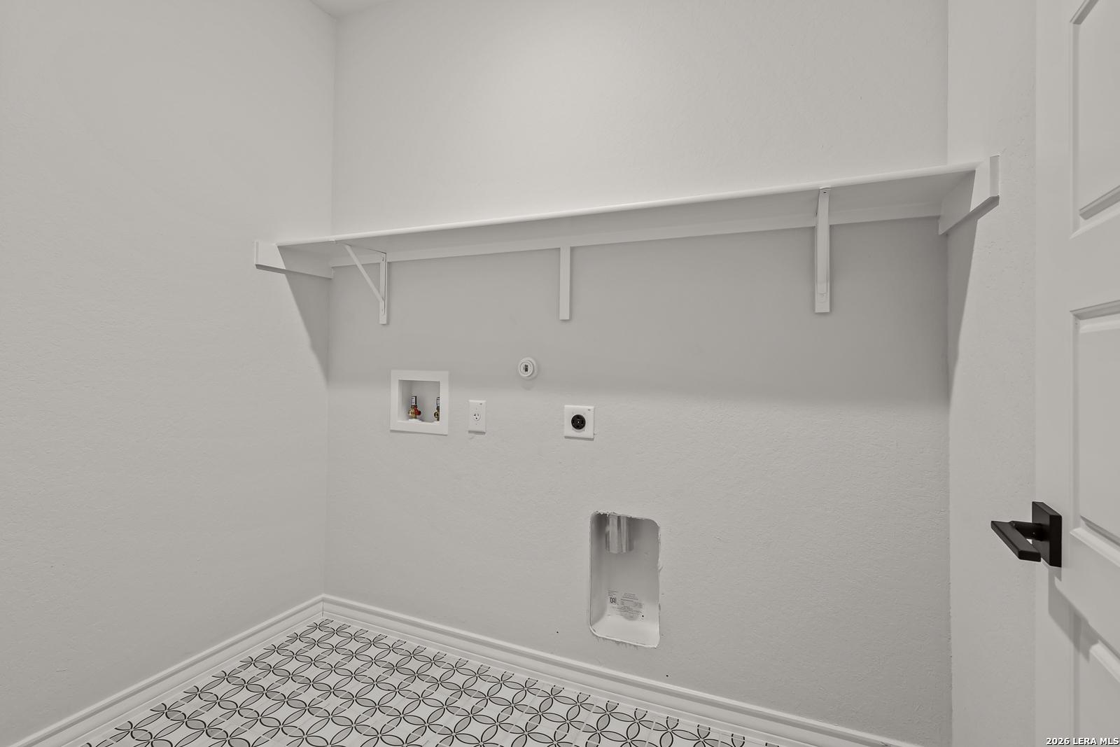 Laundry room with white shelving, patterned tile floor, and washer hookups in Davidson Homes The Oxford F, Castroville, TX