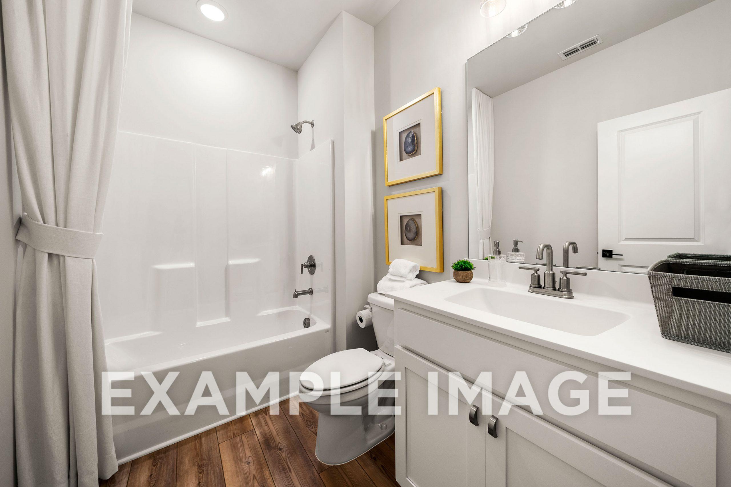 Bright bathroom in The Hickory B with white tub-shower combo, single vanity sink, toilet, and hardwood floors
