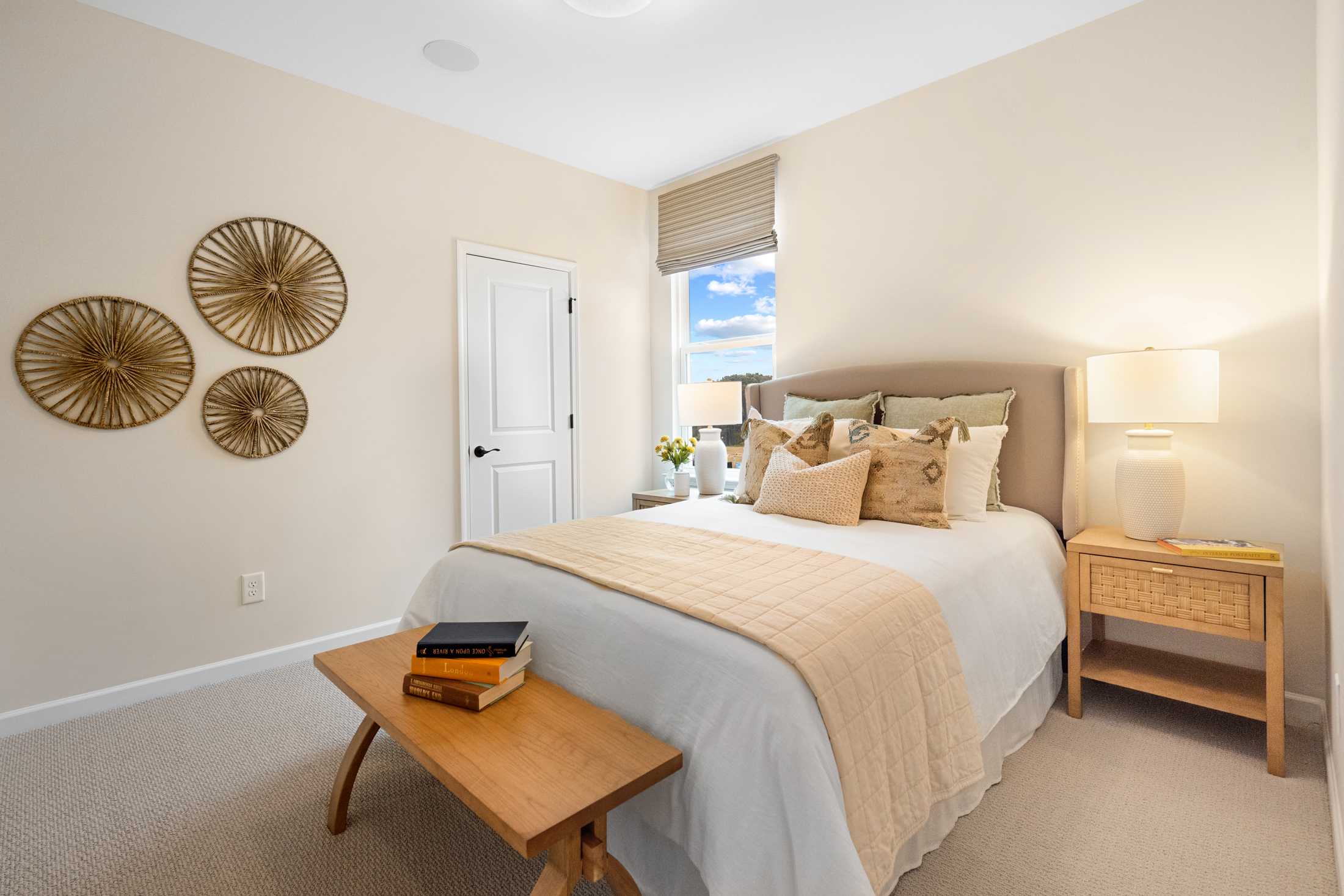 Serene master bedroom in The Edison C with rattan wall decor, upholstered bed, plush pillows, and neutral tones