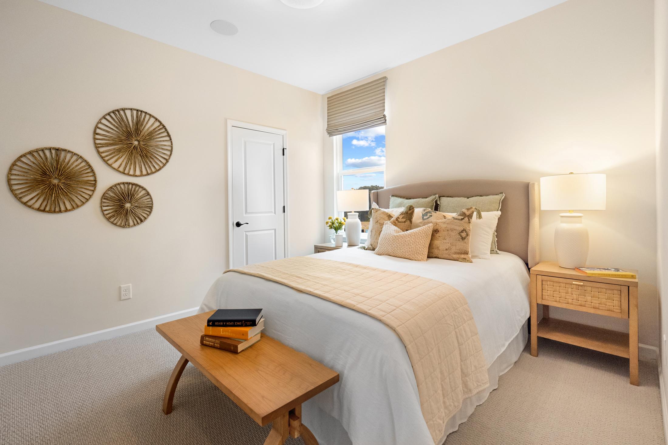 Serene master bedroom in The Edison A with neutral beige bedding, rattan wall art, upholstered headboard, and soft lamp lighting