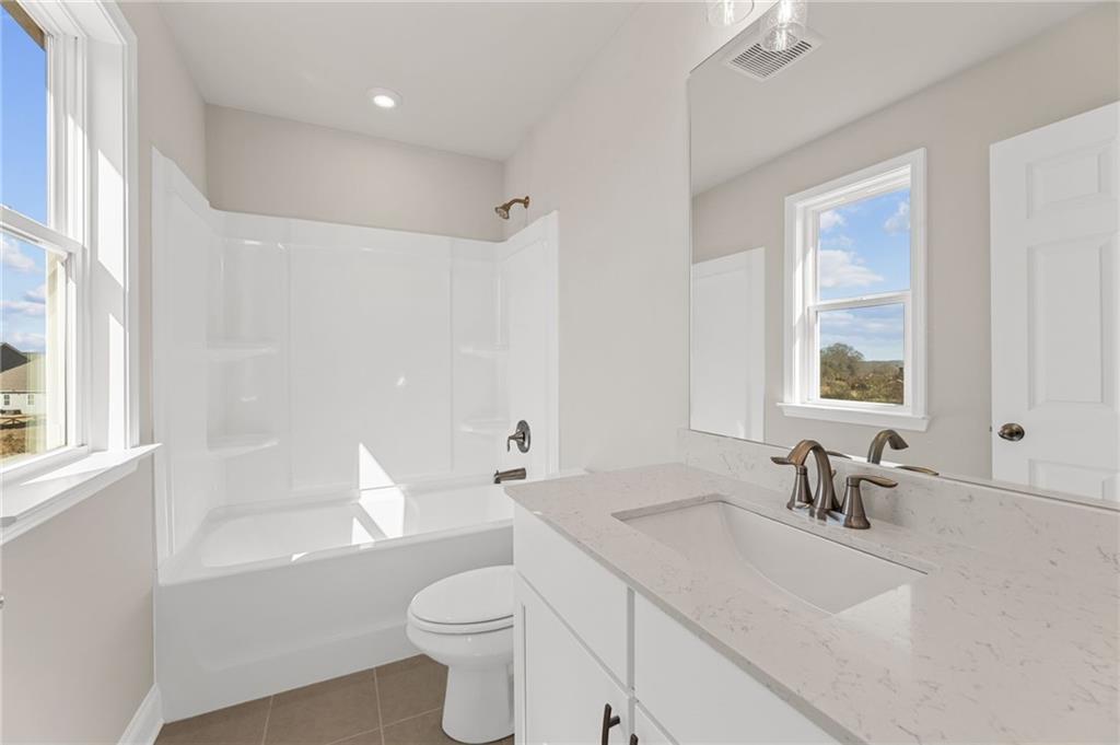 Bright bathroom featuring white subway tile tub-shower combo, quartz vanity, and natural light in Davidson Homes The Willow B, Hoschton, Georgia