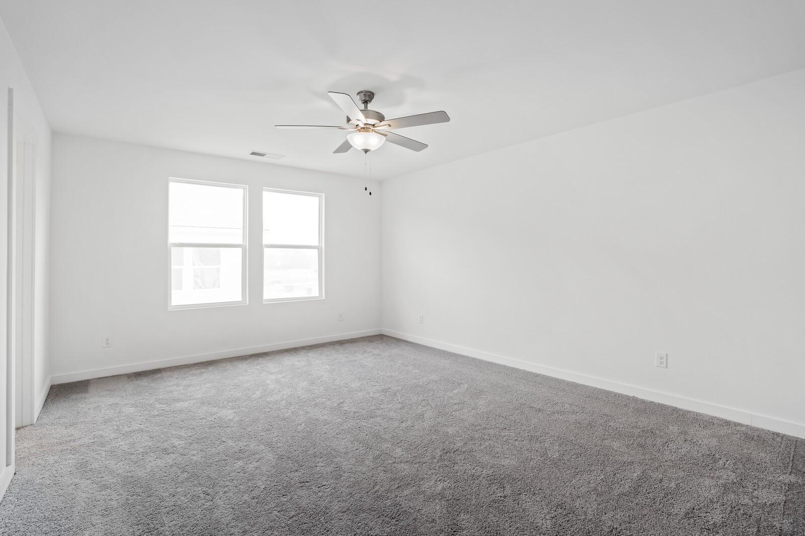 Bright, spacious bedroom with neutral carpet and ceiling fan in The Logan C floor plan at Calista Farms, White House, TN.