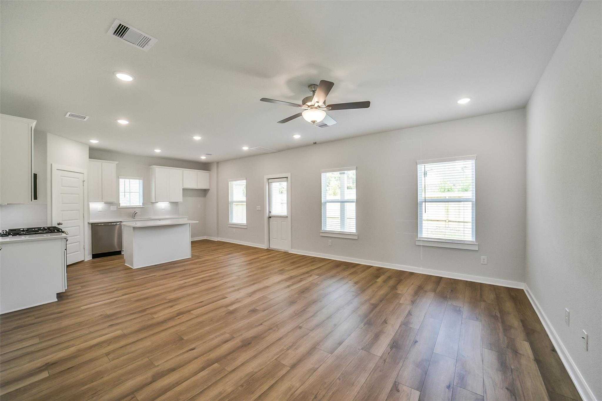 Open-concept kitchen with white cabinets, large island, stainless appliances, and hardwood floors in Davidson Homes Trinity F, Magnolia, Texas