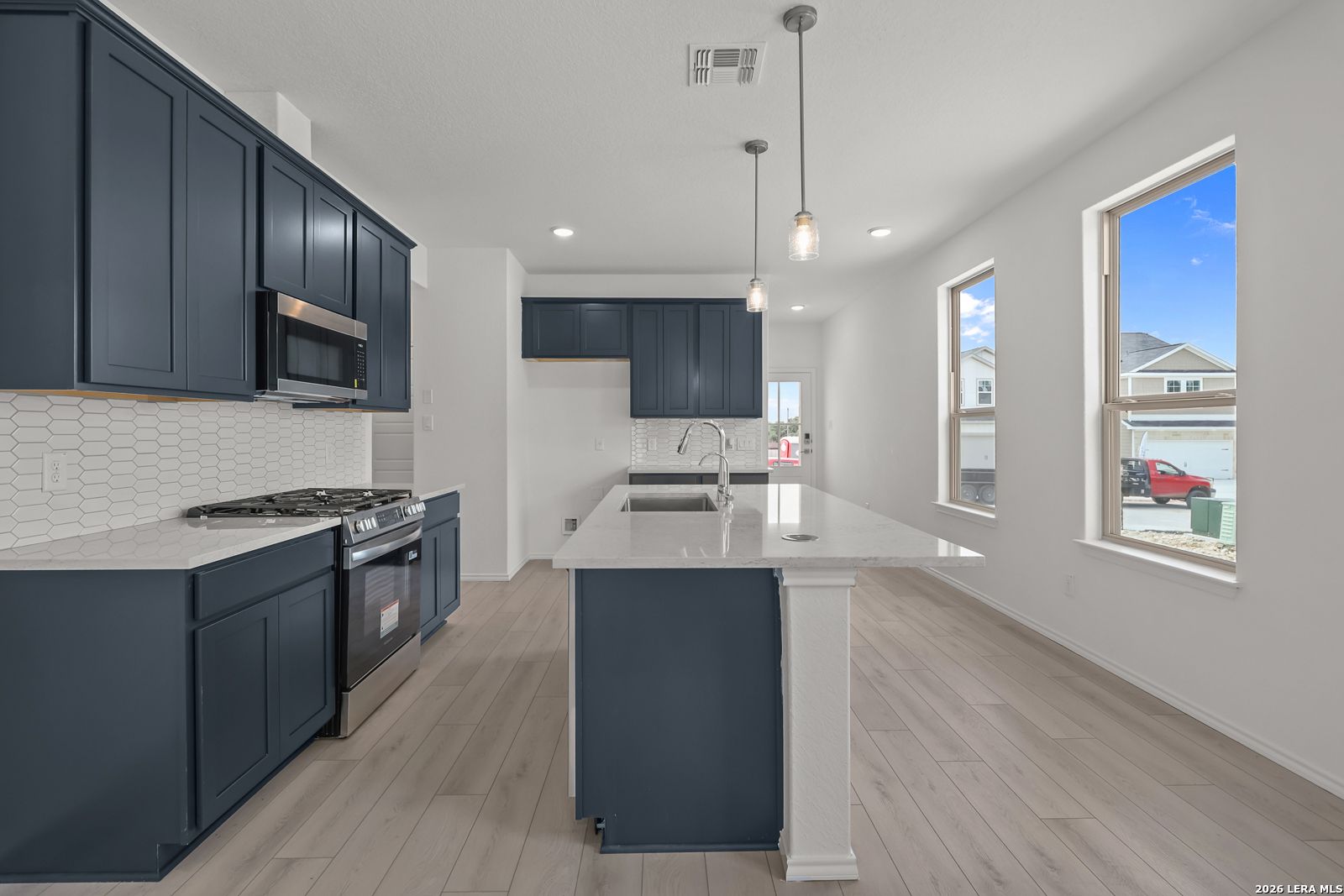 Modern kitchen with navy cabinets, white quartz island, and stainless appliances in Gillian C floor plan, San Antonio, Texas.
