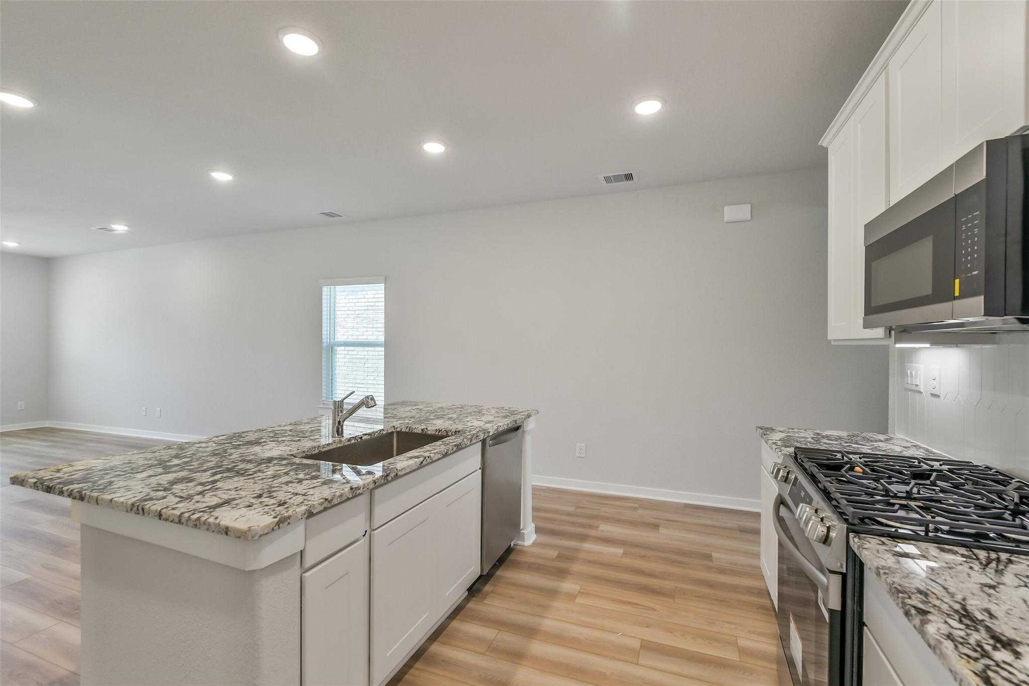 Modern kitchen with granite island, white cabinets, stainless steel appliances in 5-bedroom The Rio Grande H home, Magnolia, Texas