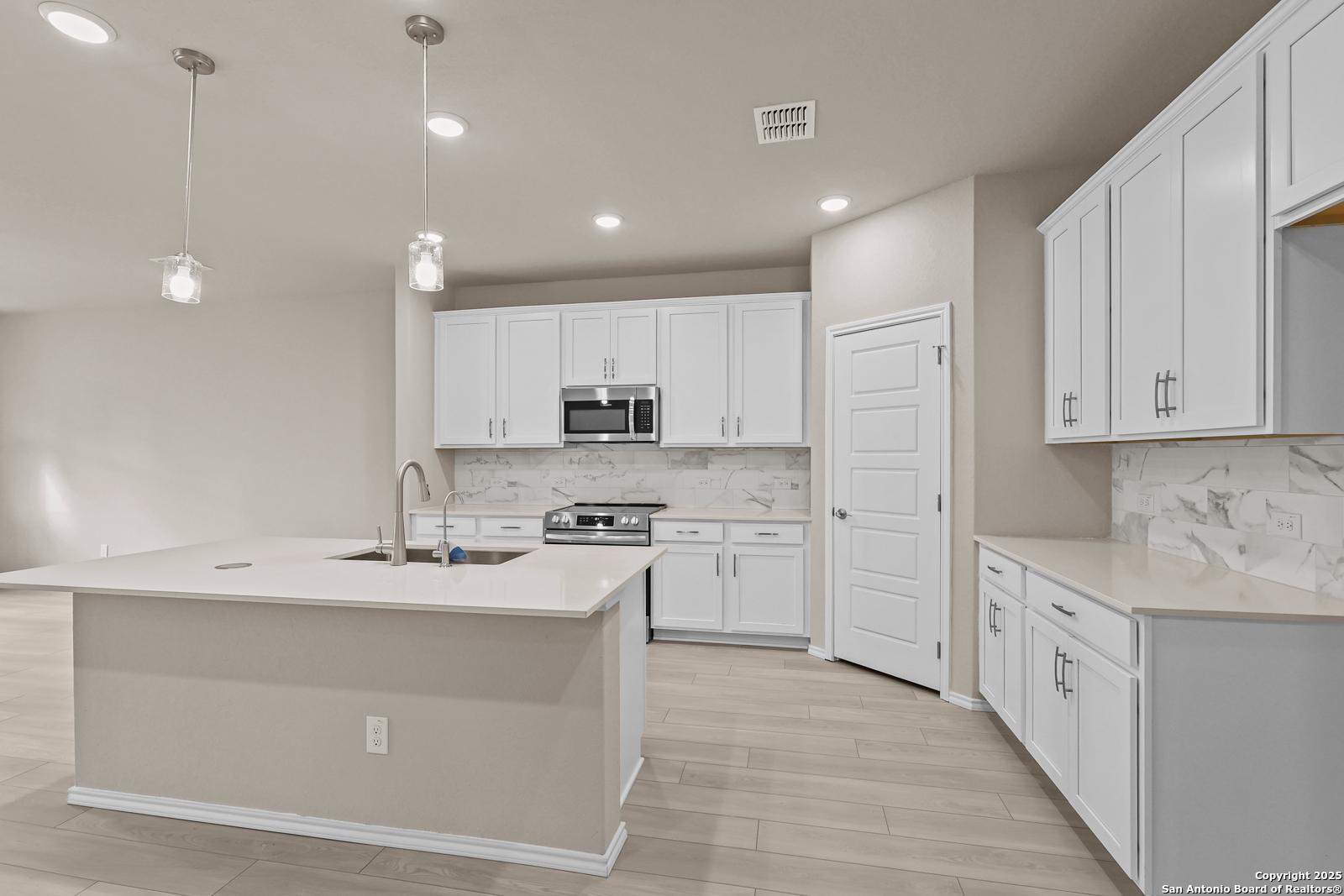 Modern white kitchen with large island, stainless steel appliances, marble subway backsplash in Davidson Homes The Douglas G, San Antonio