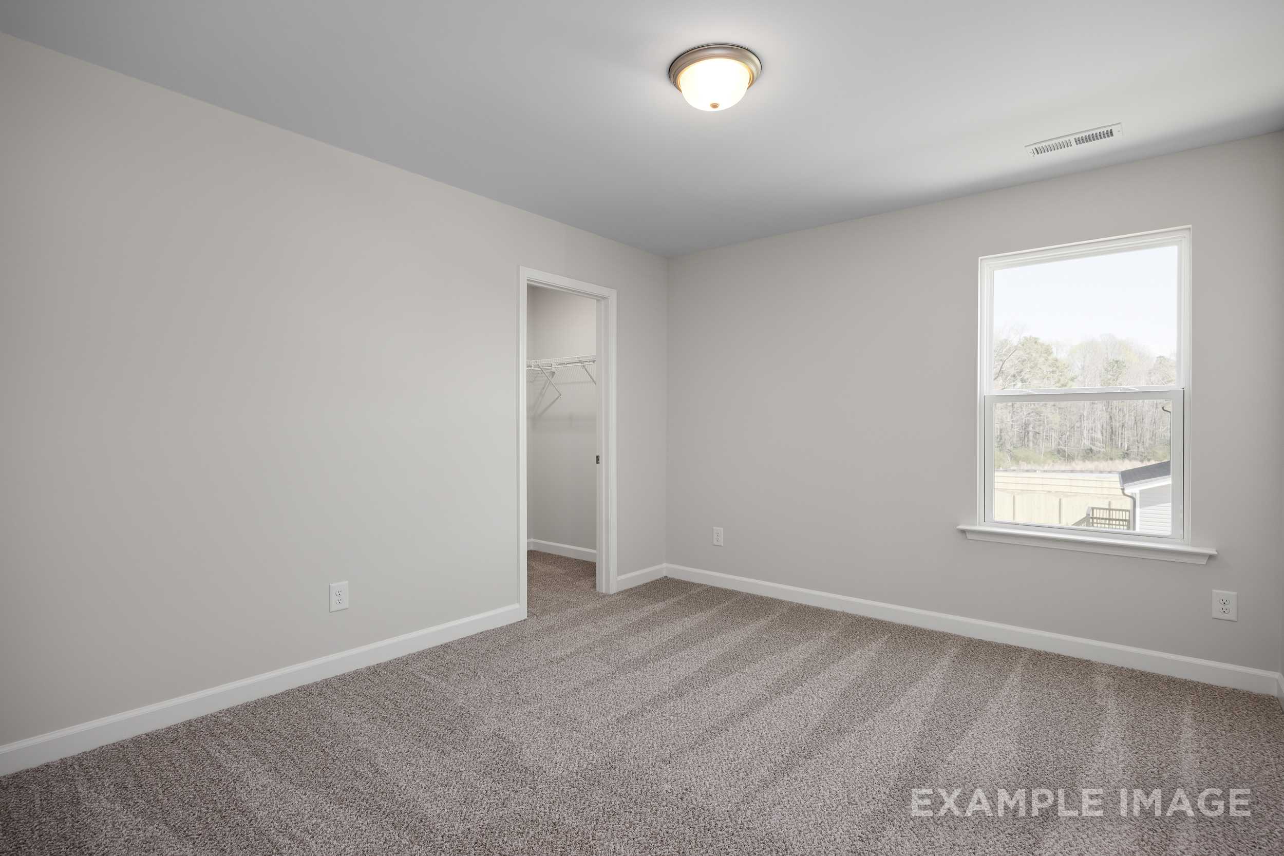 Spacious upper-floor bedroom in The Hickory II with light gray walls, carpeted floor, closet door, and large window overlooking trees
