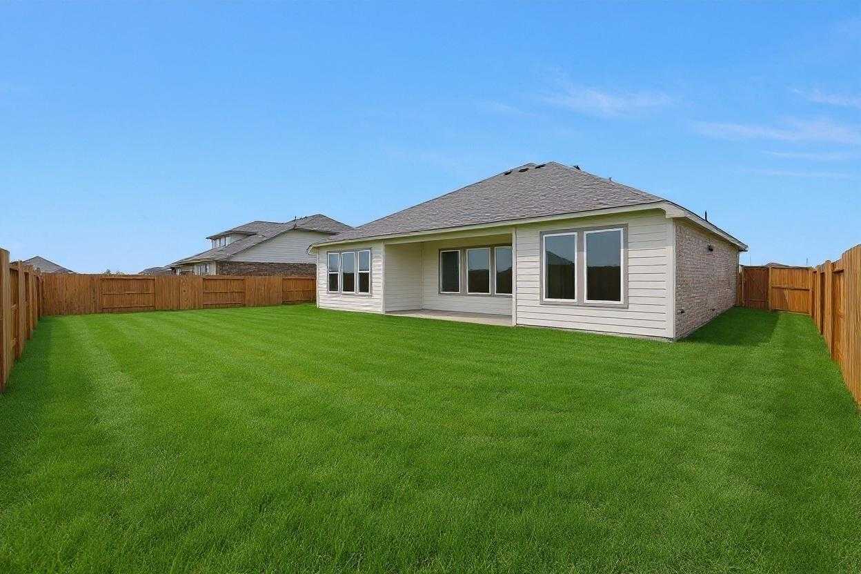 Fenced backyard with lush green lawn and covered patio on beige single-story home, The Edward A by Davidson Homes in Lago Mar, Texas City