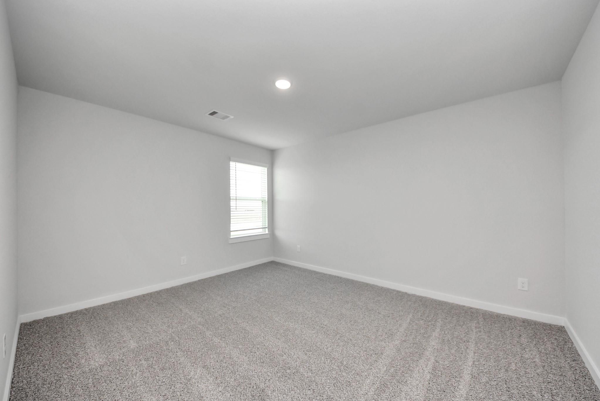 Bright empty bedroom with carpet flooring and window with blinds in Davidson Homes The San Marcos E, Beasley, Texas