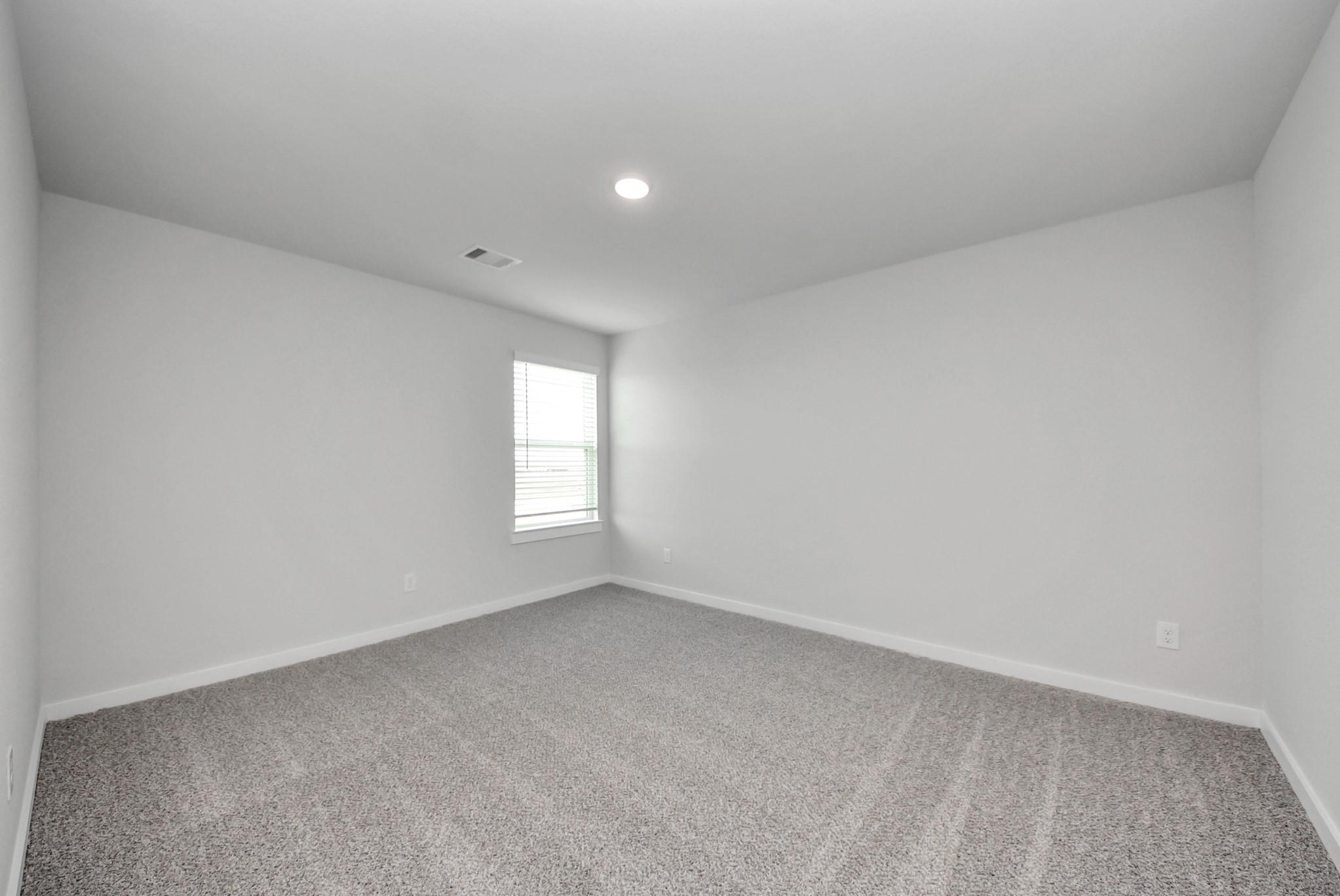 Bright empty bedroom with carpet flooring and window with blinds in Davidson Homes The San Marcos E, Beasley, Texas