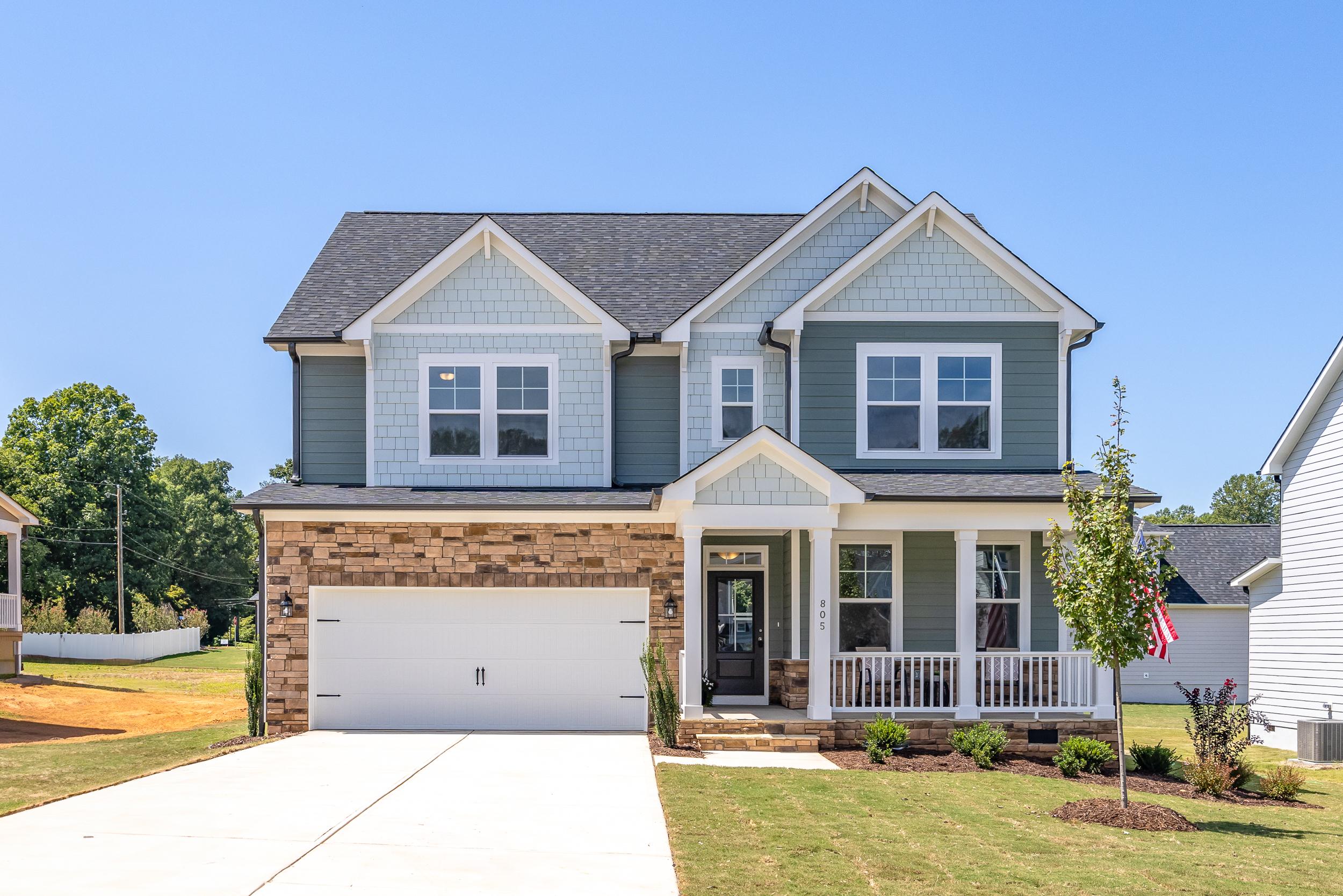 Light blue two-story craftsman home exterior at Enclave at Belmont in Belmont NC with covered porch, brick garage, and landscaped yard