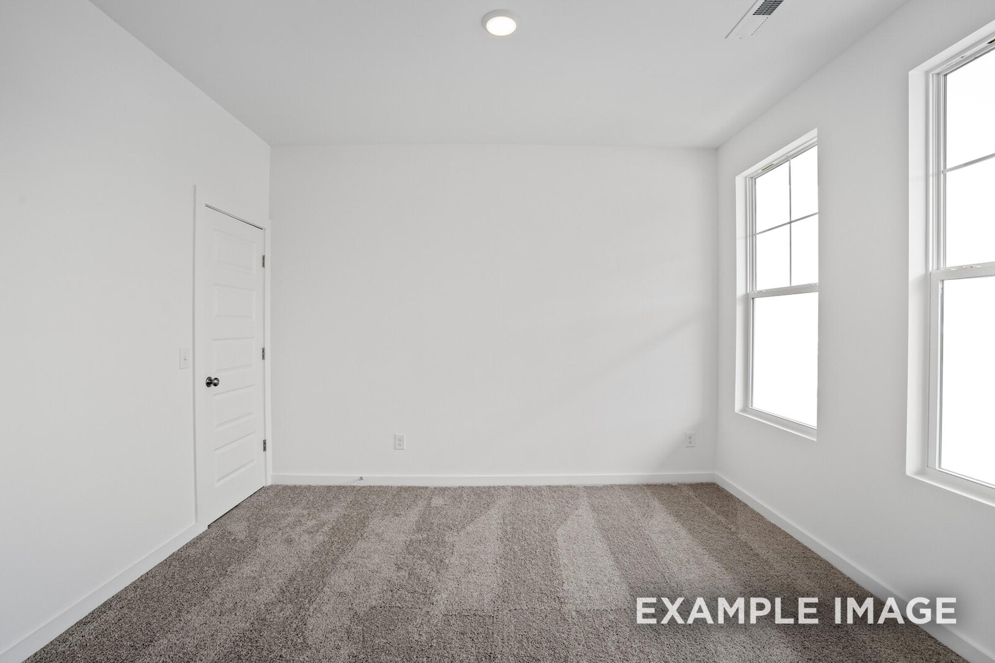 Spacious empty master bedroom in The Logan C with white walls, large double windows, and beige carpet floor