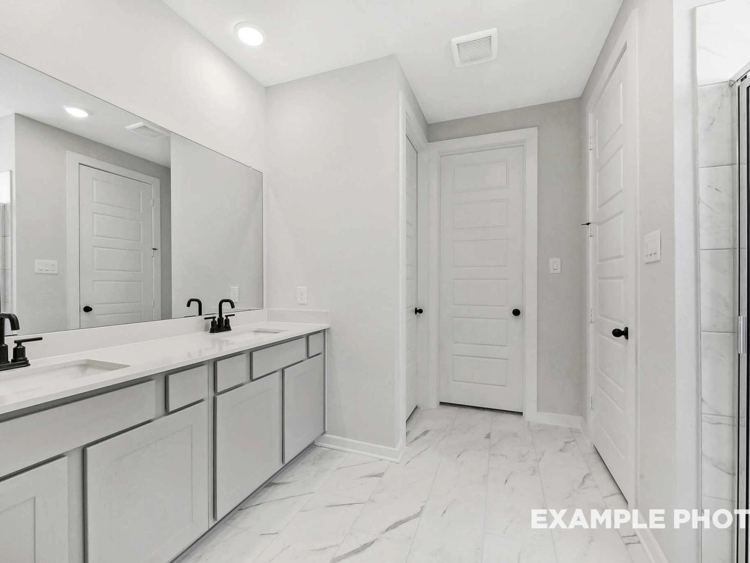 Modern primary bathroom with double vanity, marble-style tile, and black fixtures in The Sequoia C at Sundance Cove.