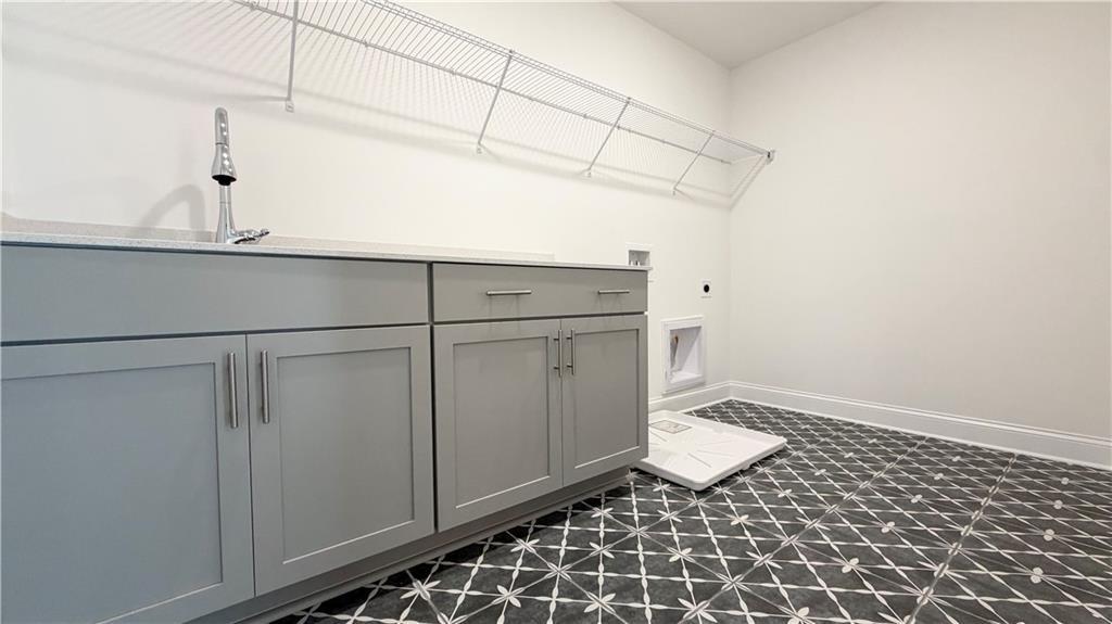 Modern laundry room with gray cabinets, utility sink, and patterned tile flooring in The Hickory C home at Wehunt Meadows.