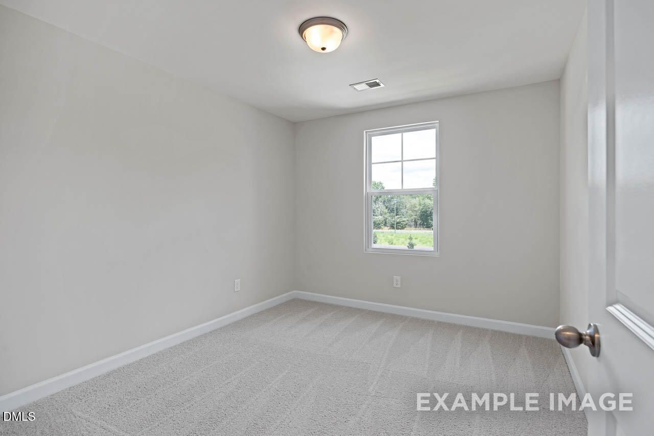 Bright, carpeted secondary bedroom with neutral walls in The Graham floor plan at Springvale, Fuquay-Varina, North Carolina.