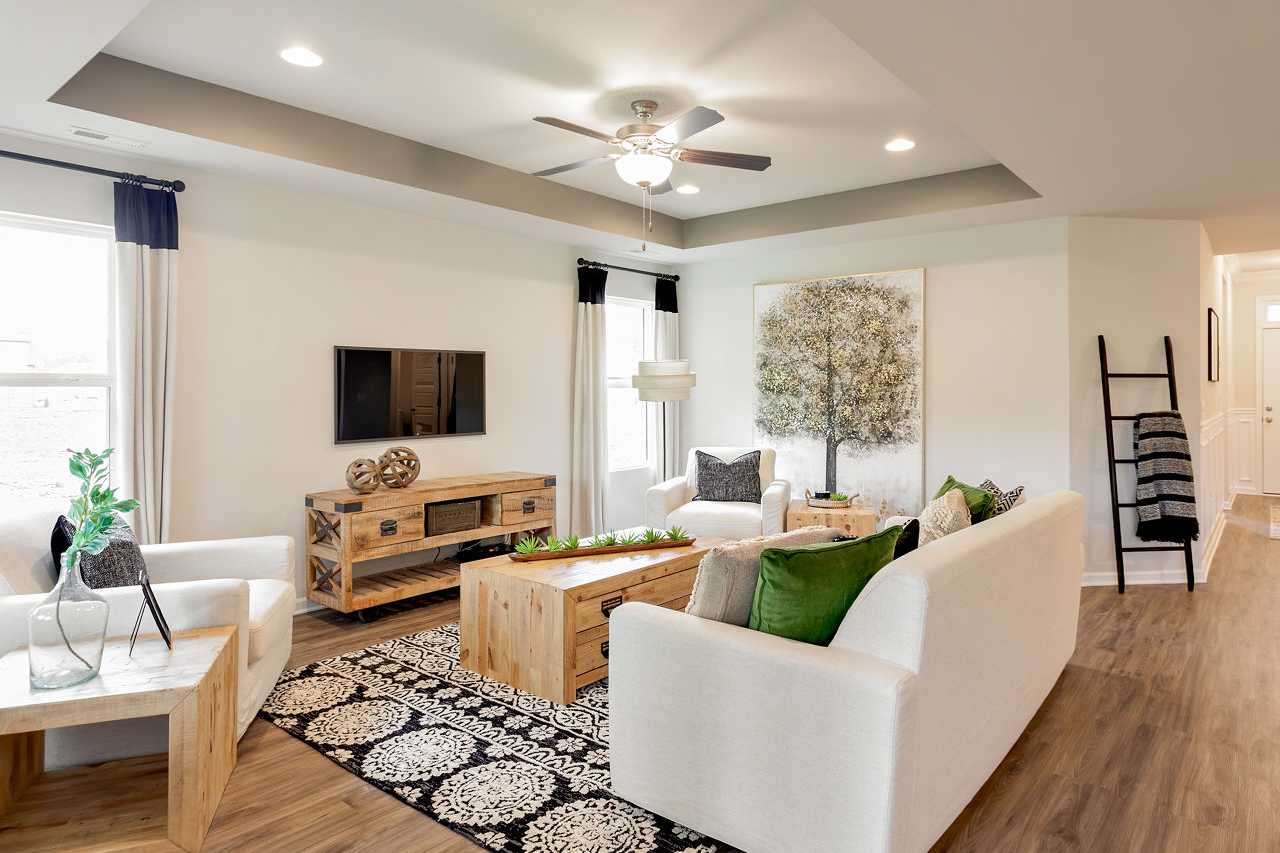 Spacious living room in The Franklin home with white sofas, wooden console, tree wall art, and neutral decor