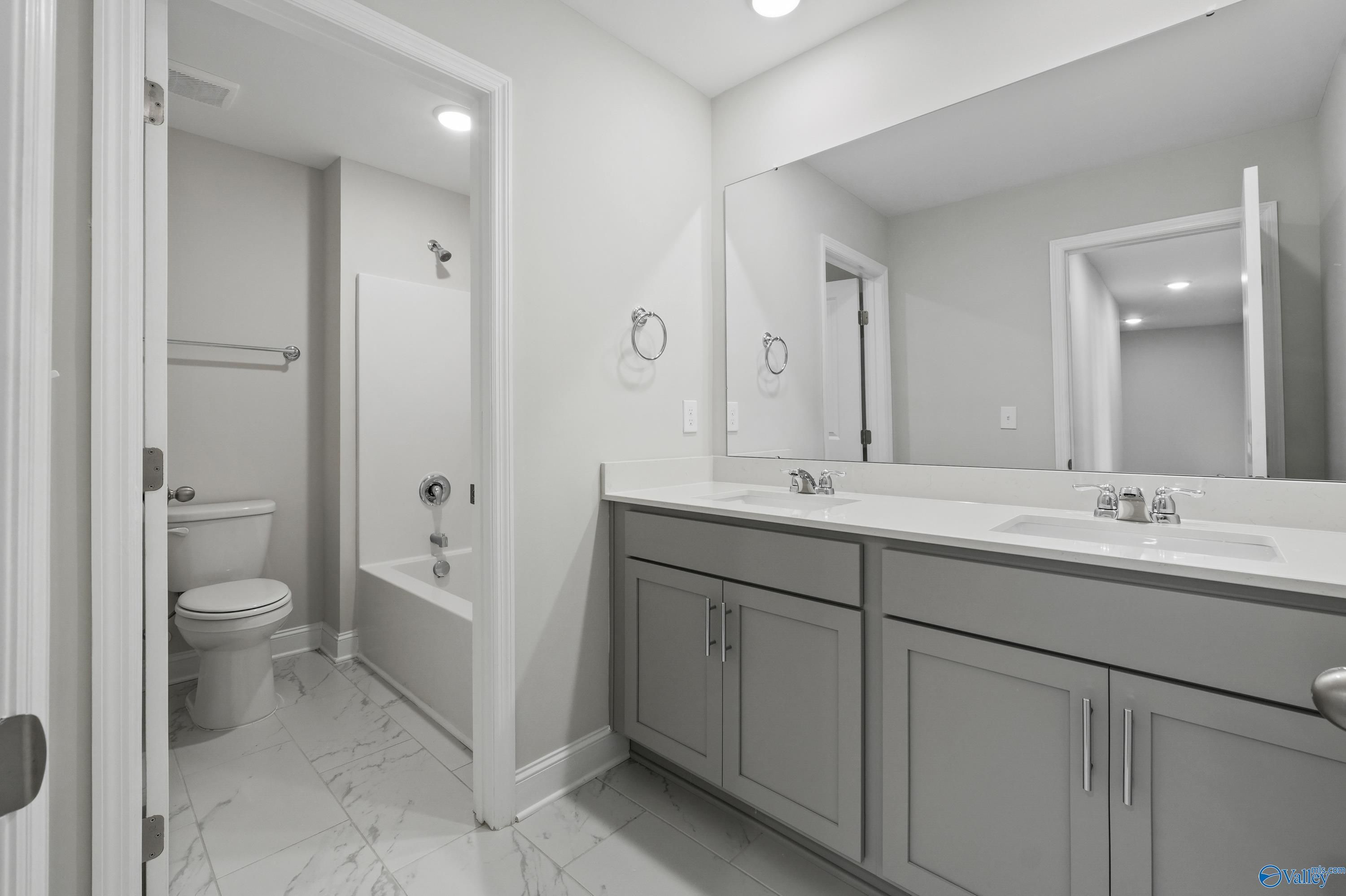 Elegant master bathroom with double vanity, gray cabinets, alcove tub shower, and tile floor in Davidson Homes The Camden B, Huntsville