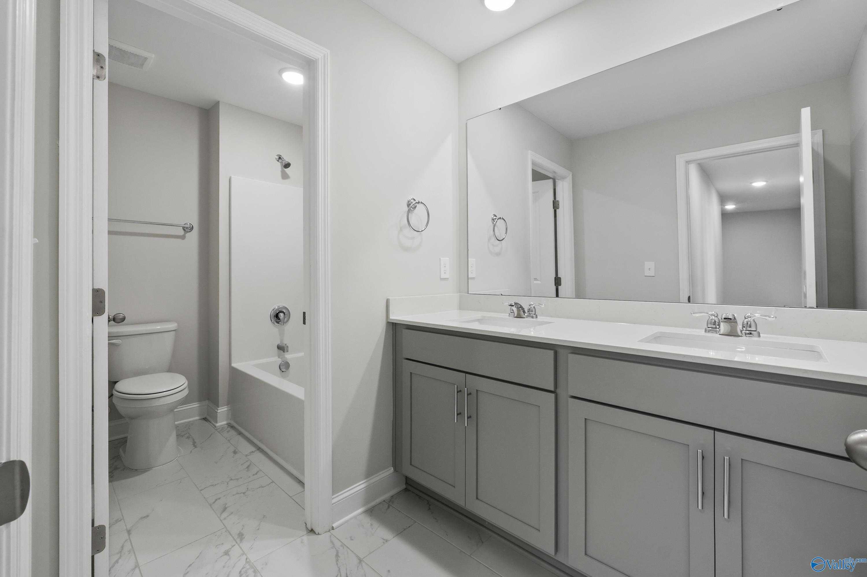 Elegant master bathroom with double vanity, gray cabinets, alcove tub shower, and tile floor in Davidson Homes The Camden B, Huntsville