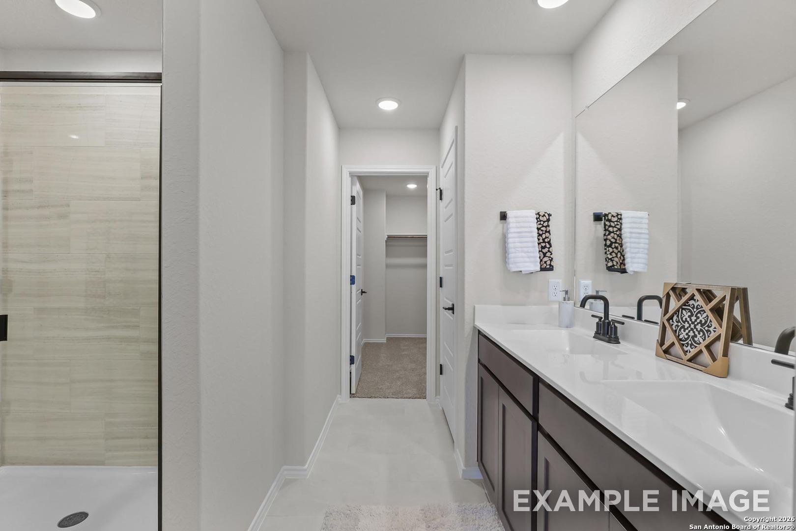 Modern master bathroom featuring double vanity, frameless glass shower, and large mirror in Davidson Homes The Trinity B, San Antonio