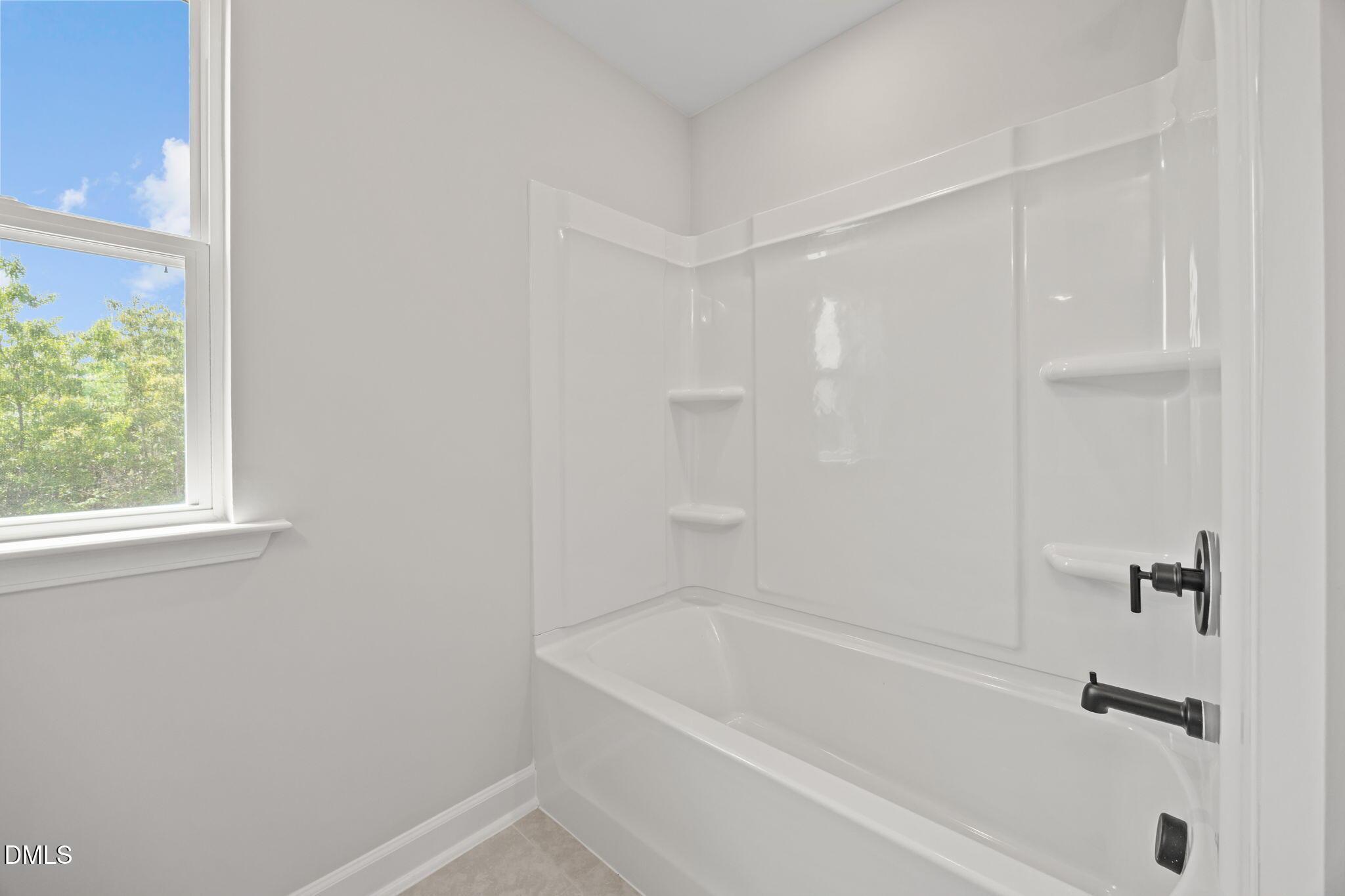 Bright white bathtub shower combo with shelves and black fixtures in Davidson Homes The Willow D, Wendell, North Carolina