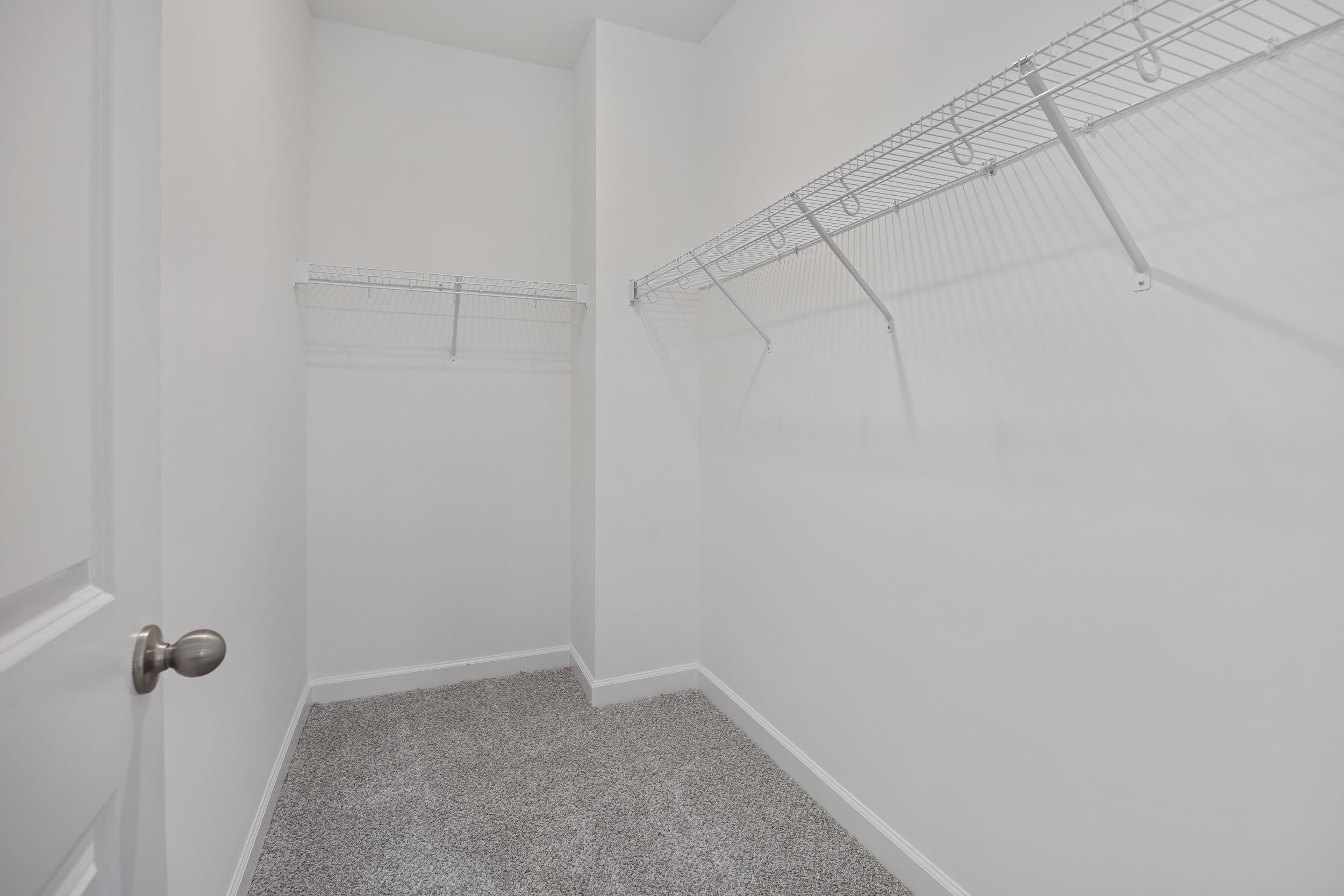 Walk-in closet at Gregory Village in Lillington, NC by Davidson Homes with white shelving and neutral carpeting.