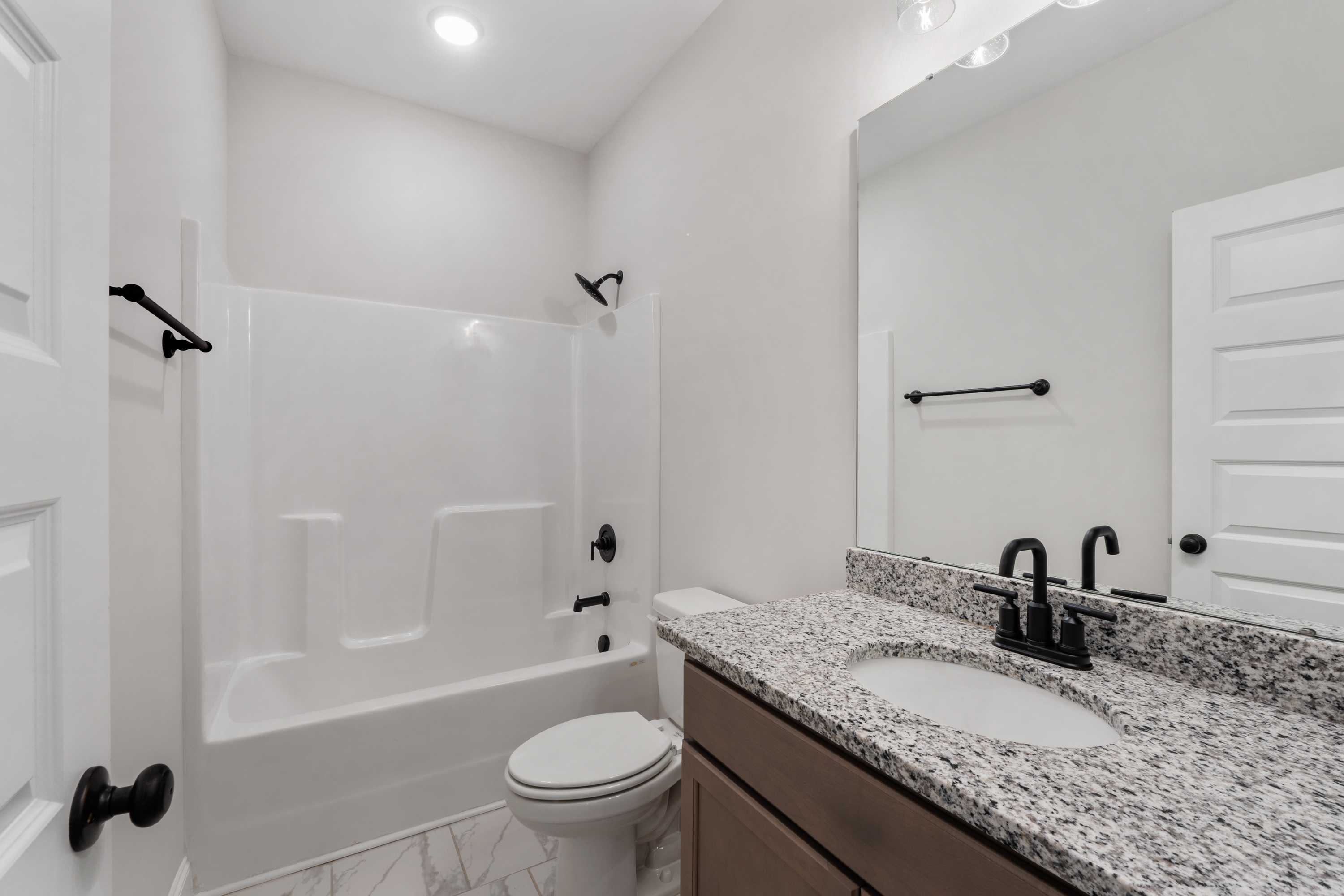 Modern master bathroom in The Oxford by Davidson Homes: granite vanity, deep tub with white tile surround, black fixtures