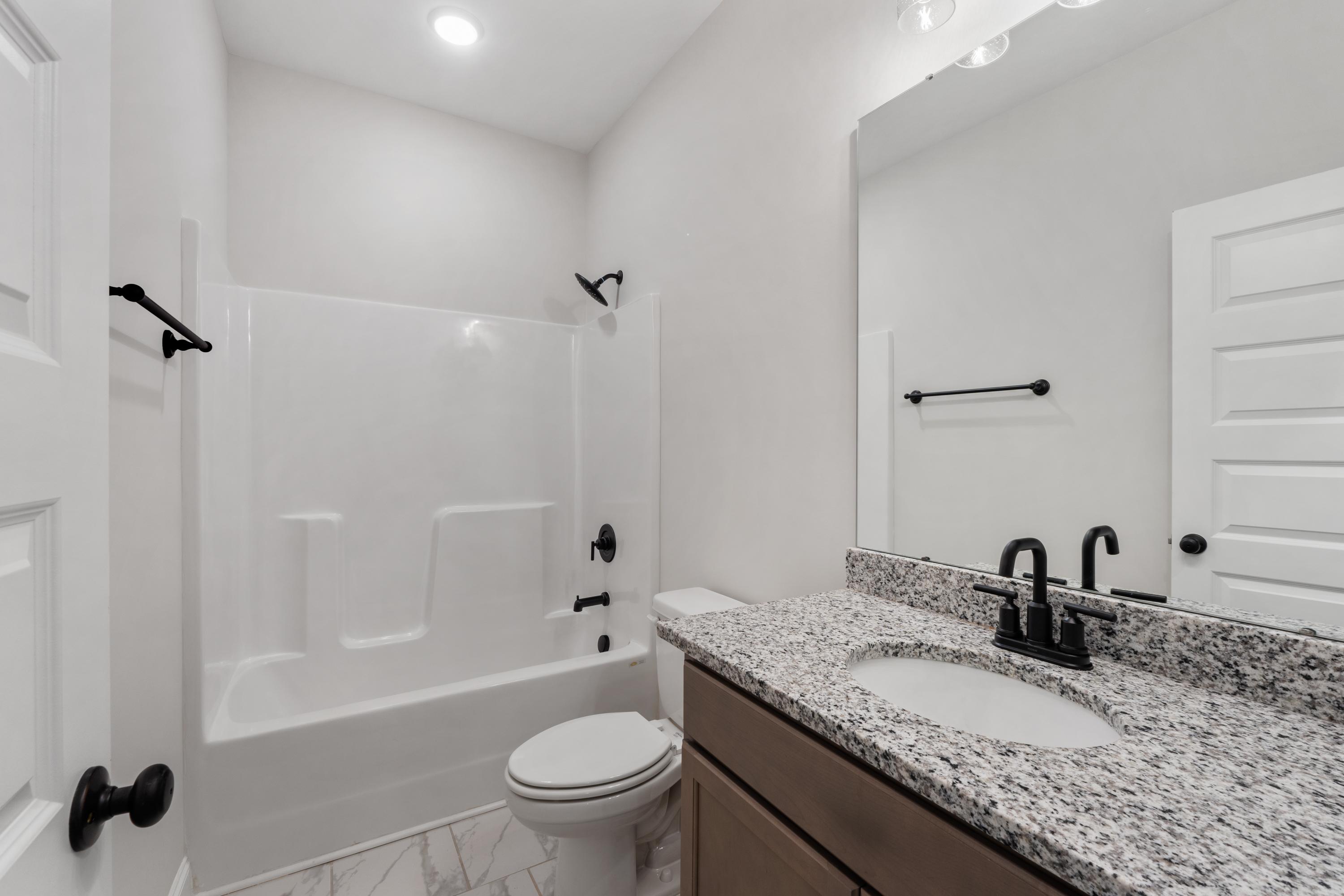 Modern master bathroom in The Oxford by Davidson Homes: granite vanity, deep tub with white tile surround, black fixtures