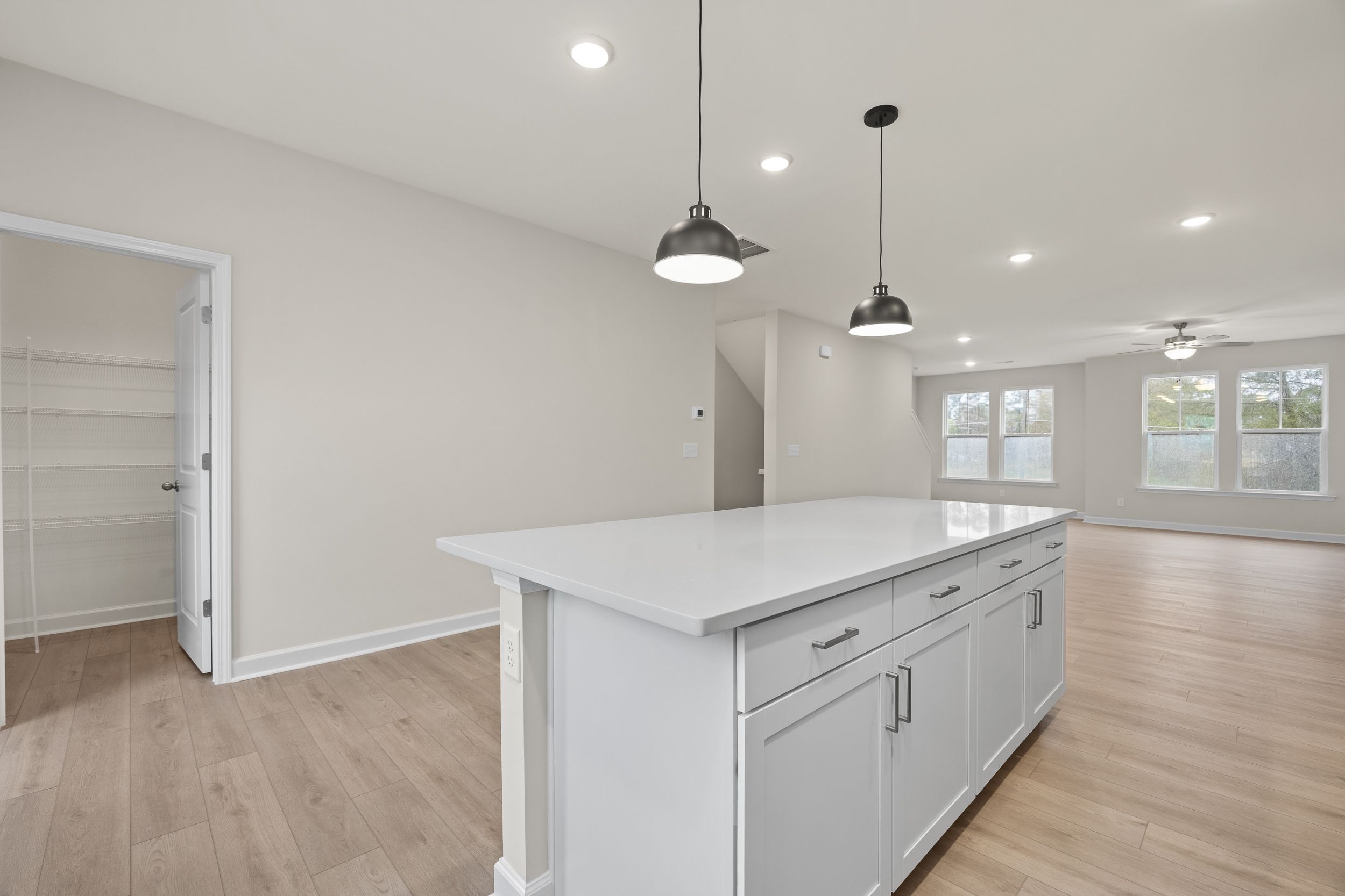 Spacious kitchen with white island, pendant lights, hardwood floors, and open pantry at Forestville Yard Townhomes in Knightdale NC