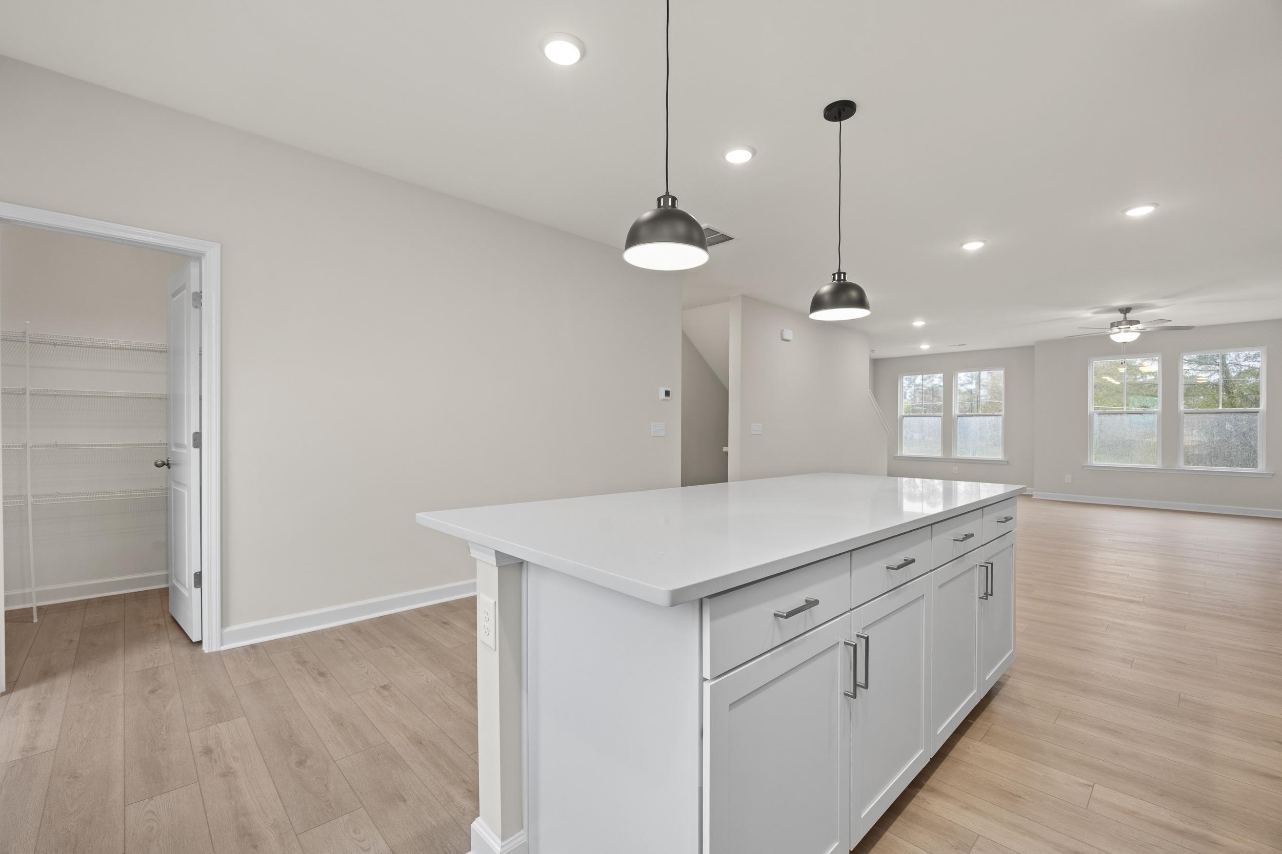 Spacious kitchen with white island, pendant lights, hardwood floors, and open pantry at Forestville Yard Townhomes in Knightdale NC