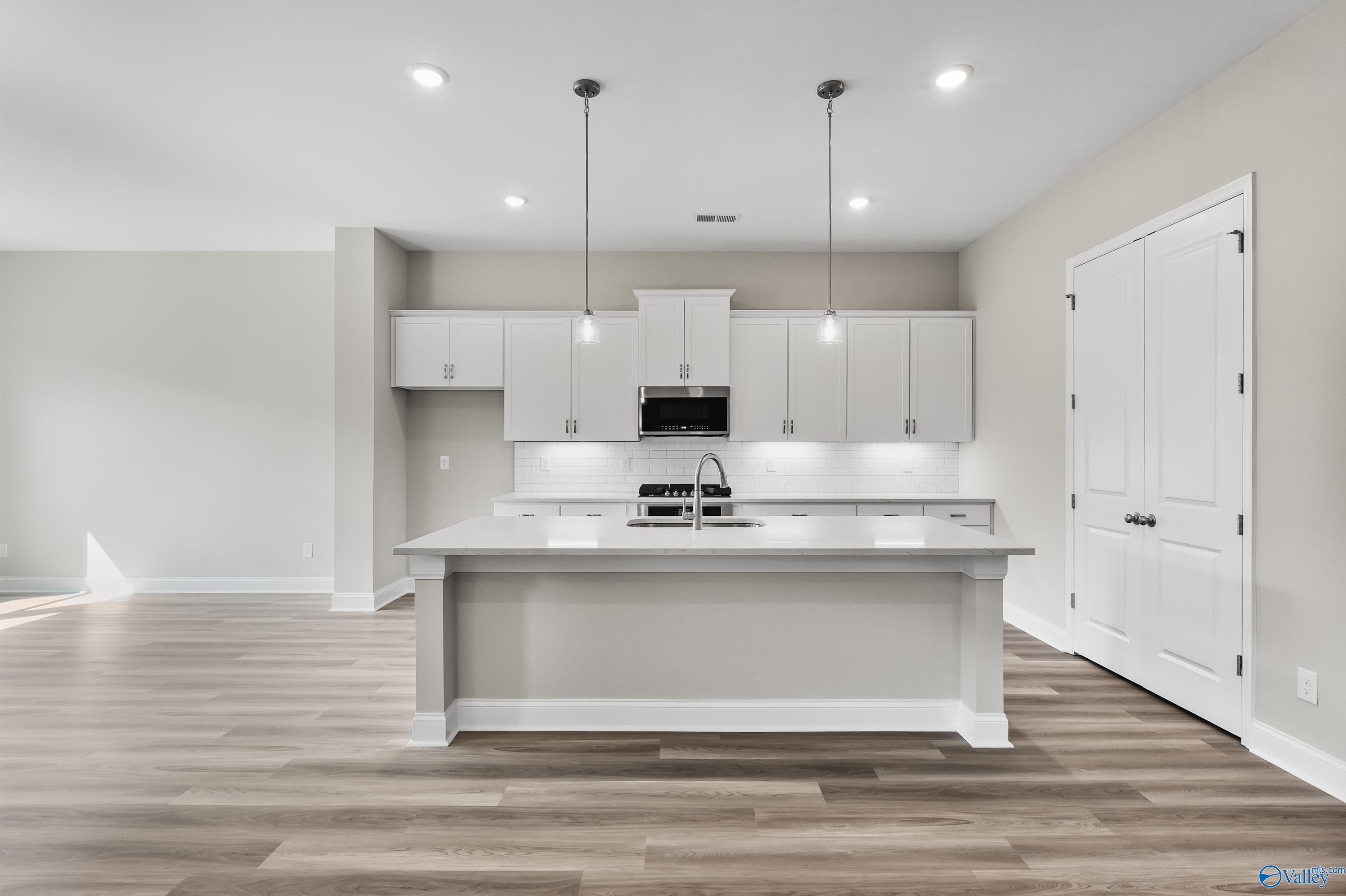 Spacious modern kitchen with white shaker cabinets, large center island sink, stainless appliances in Evermore Homes The Haven, Owens Cross Roads, AL