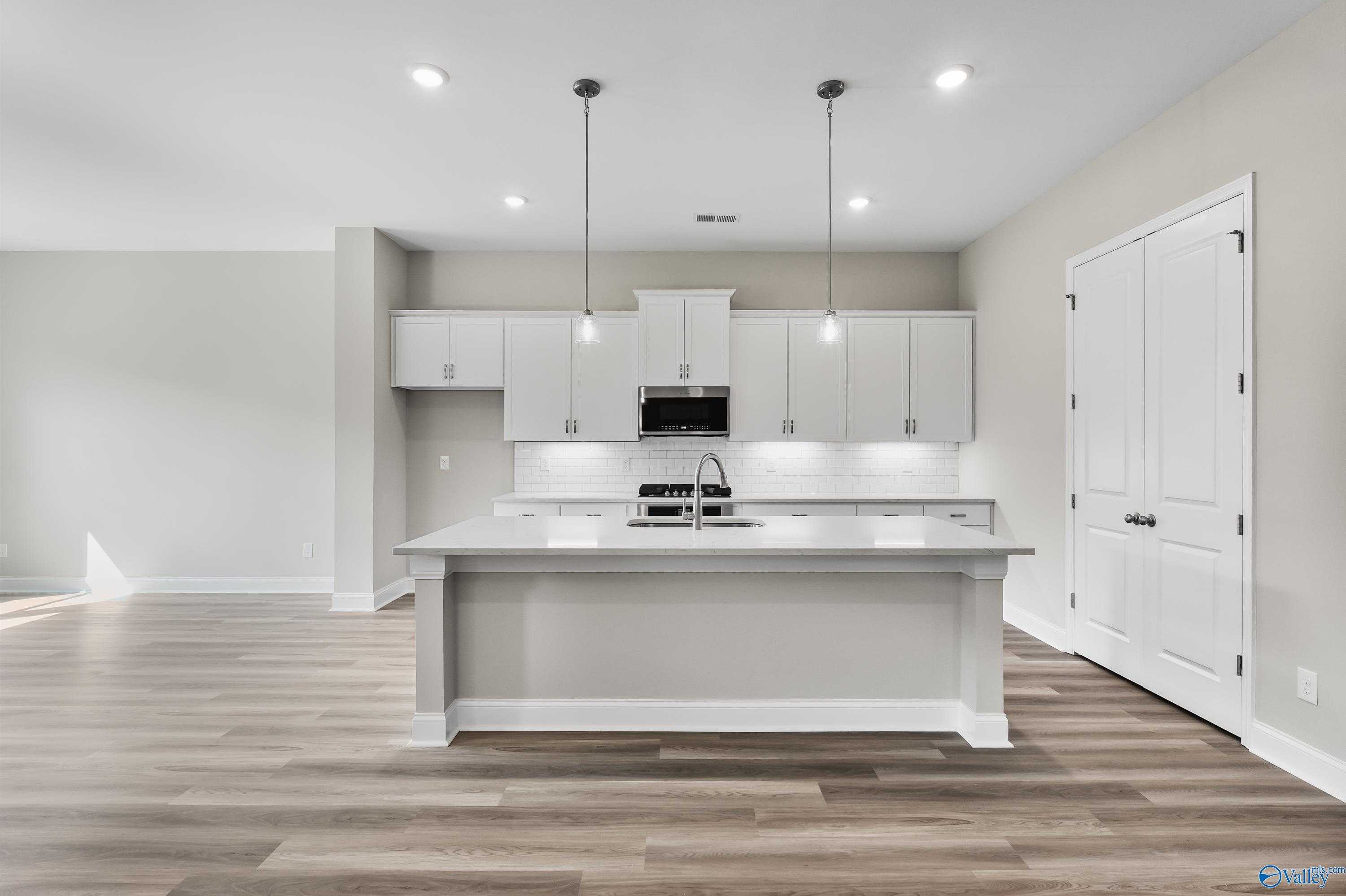 Spacious modern kitchen with white shaker cabinets, large center island sink, stainless appliances in Evermore Homes The Haven, Owens Cross Roads, AL