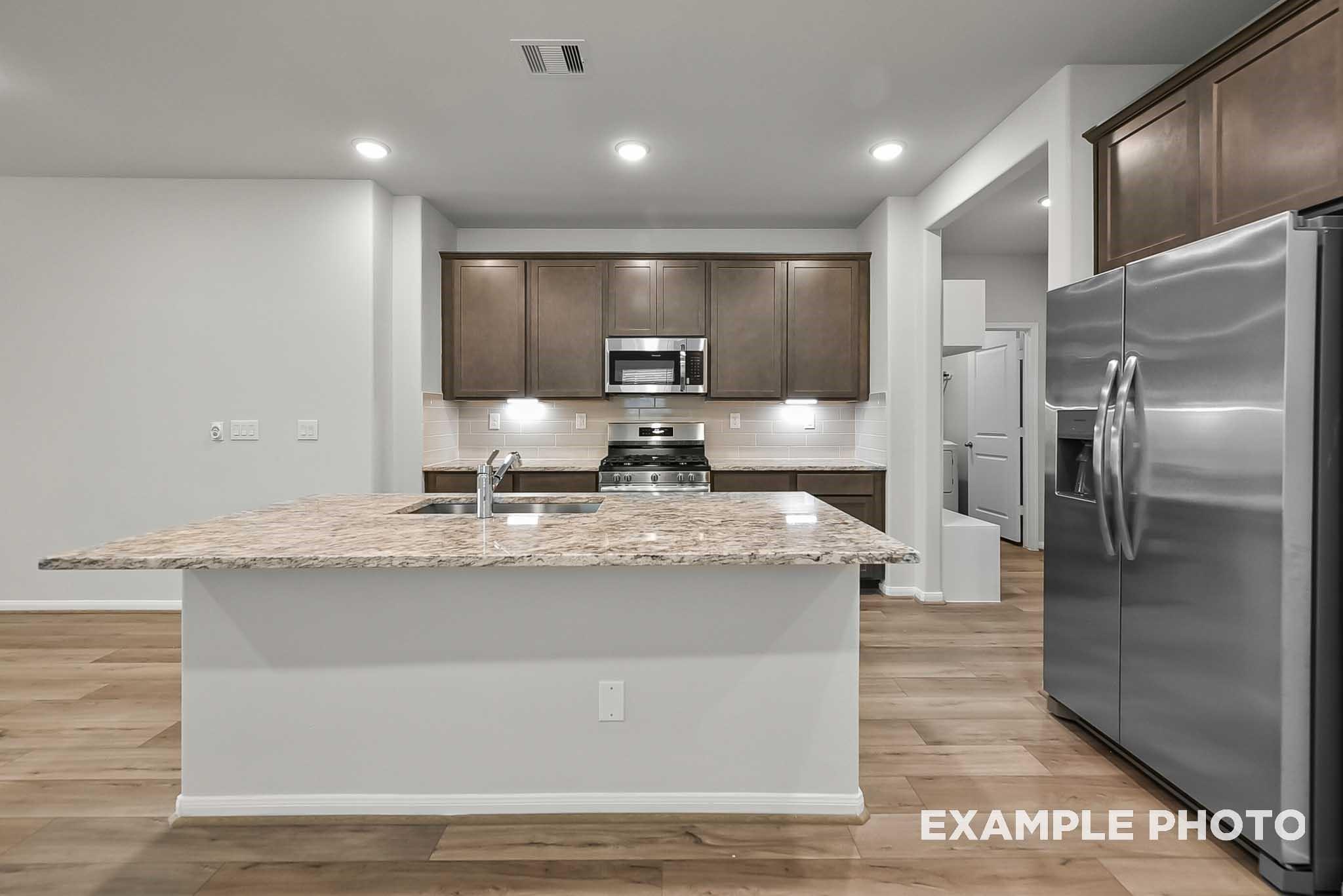 Modern kitchen with granite island and stainless steel appliances in The Blanco F plan at Spring Branch Crossing, Conroe.