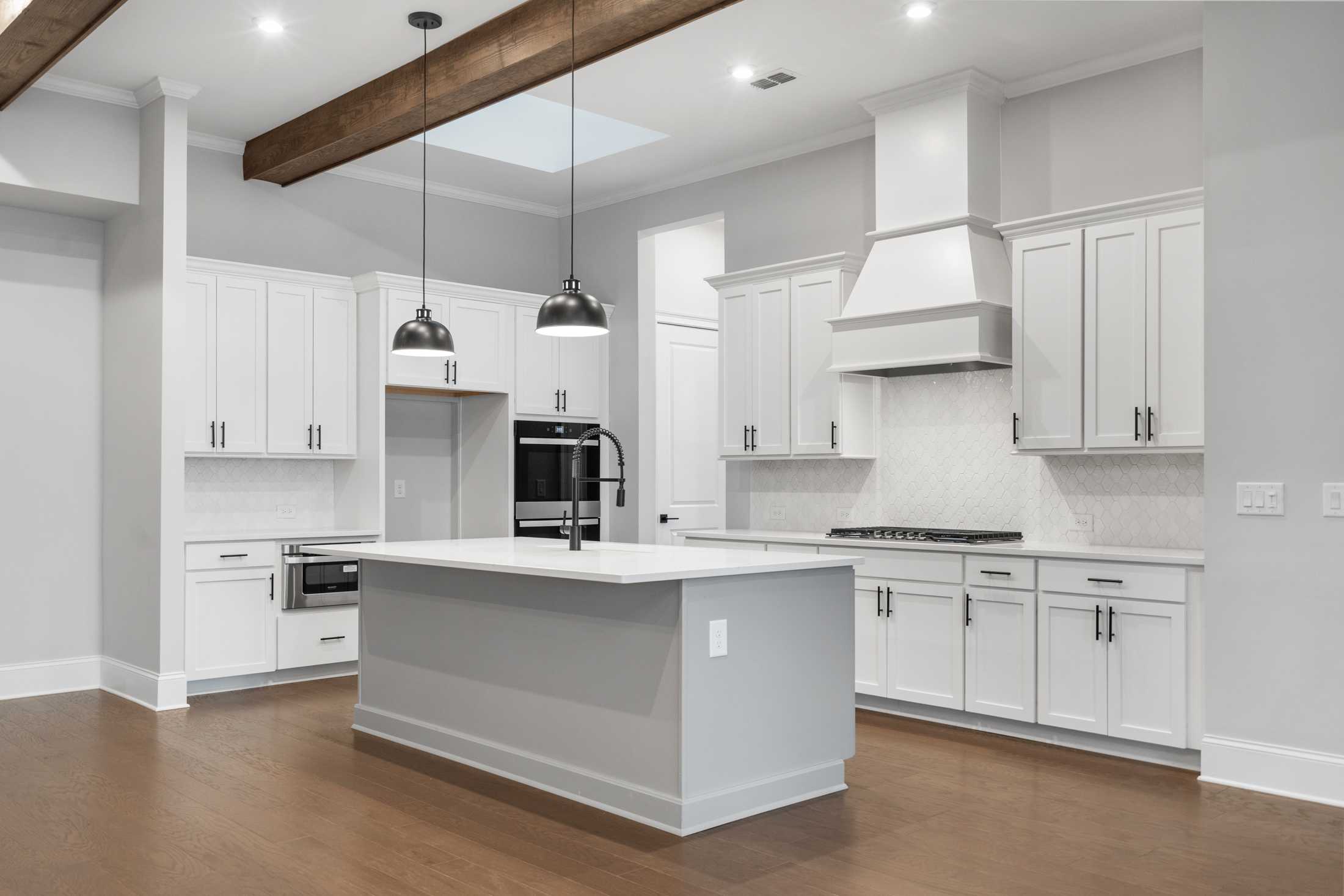 Gourmet kitchen in The Seaside by Davidson Homes featuring white shaker cabinets, gray quartz island, stainless appliances, and wood beam ceiling